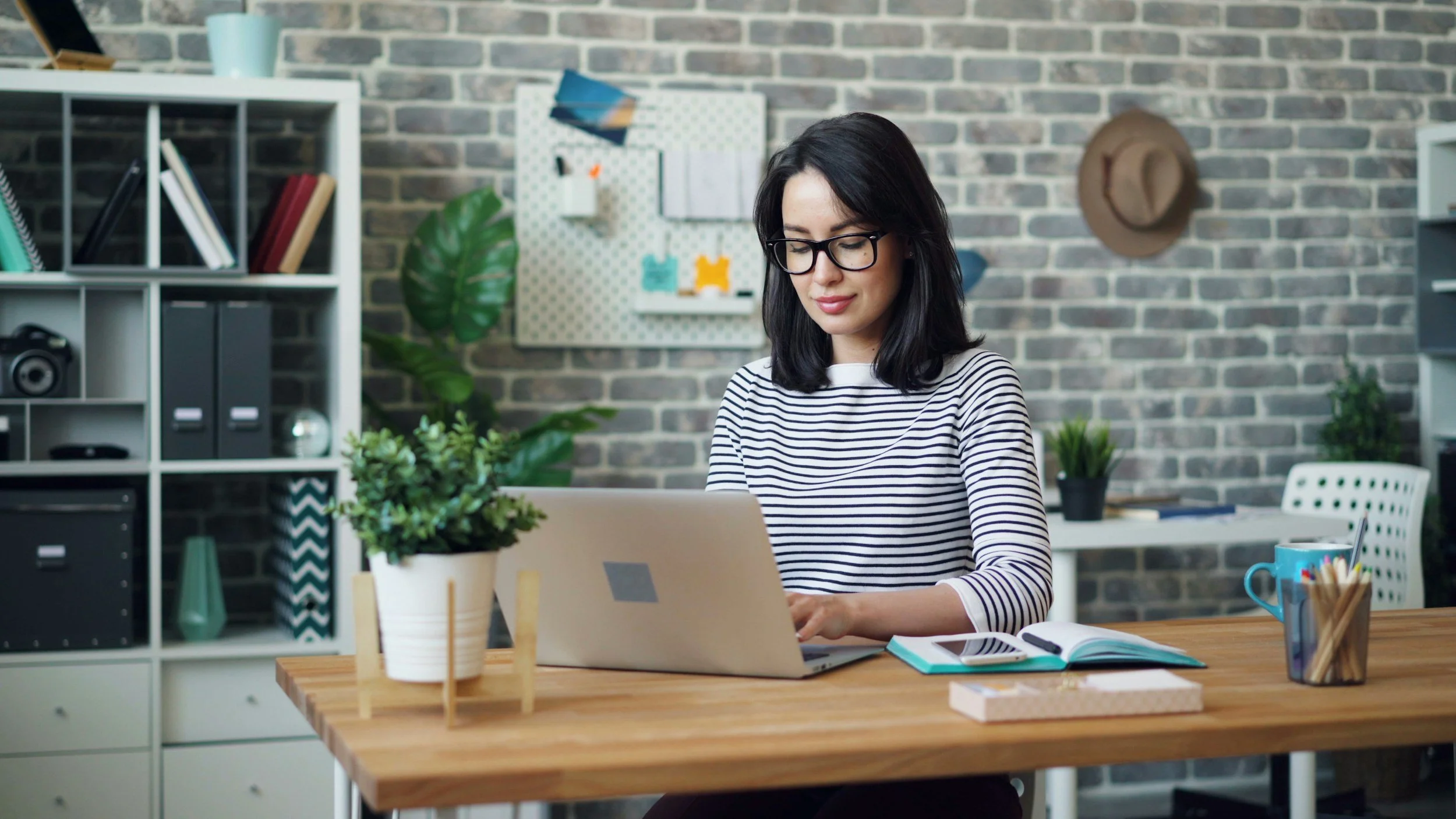 confident smiling woman in her 30s-40s sitting at a cozy desk, looking at her laptop with budgeting spreadsheet open.