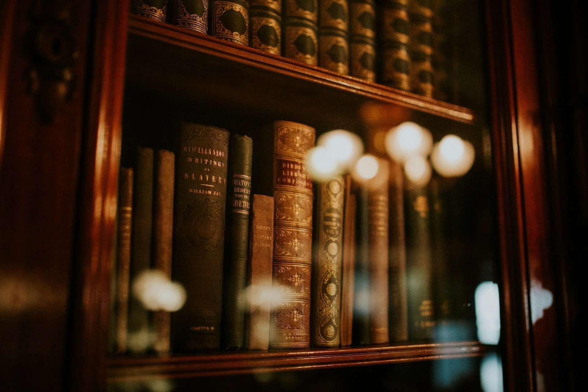 A locked wooden bookcase with glass doors containing old, leather-bound books with ornate designs.