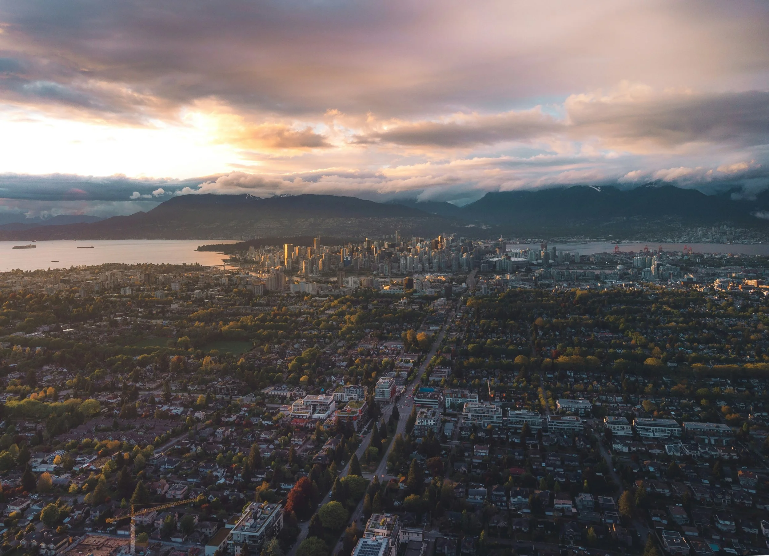 An aerial view of a city at sunset with a river and mountain range in the background.