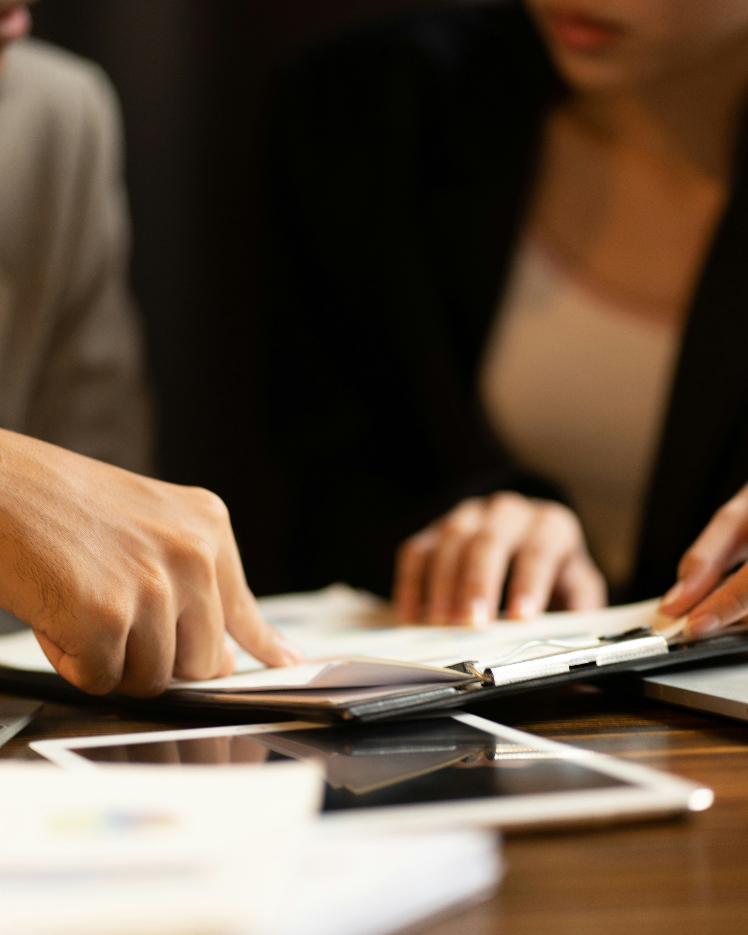 Two people reviewing documents or a planner on a desk with tablets and papers.
