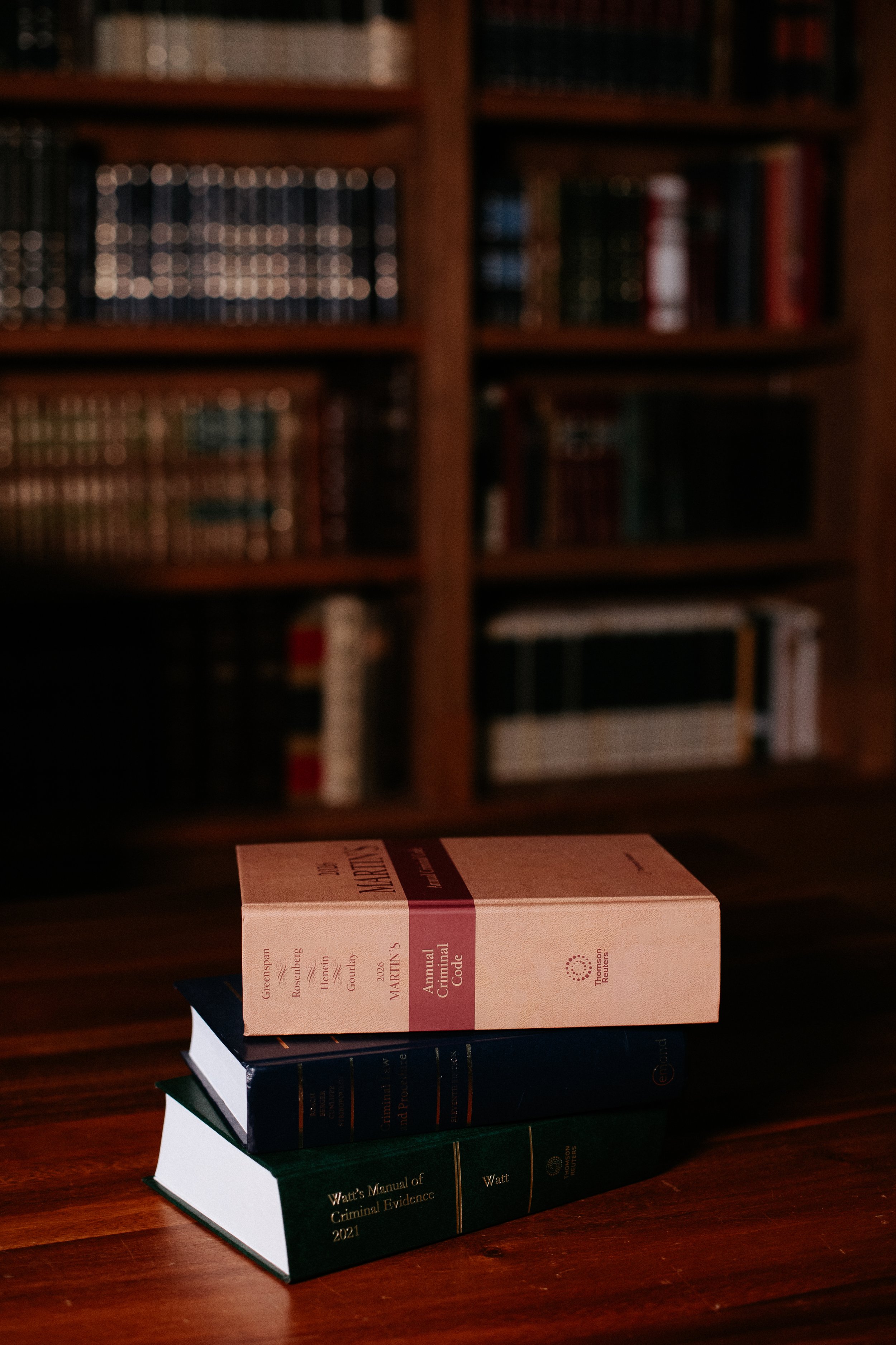 A stack of three law books on a wooden table in front of a bookshelf filled with various books.
