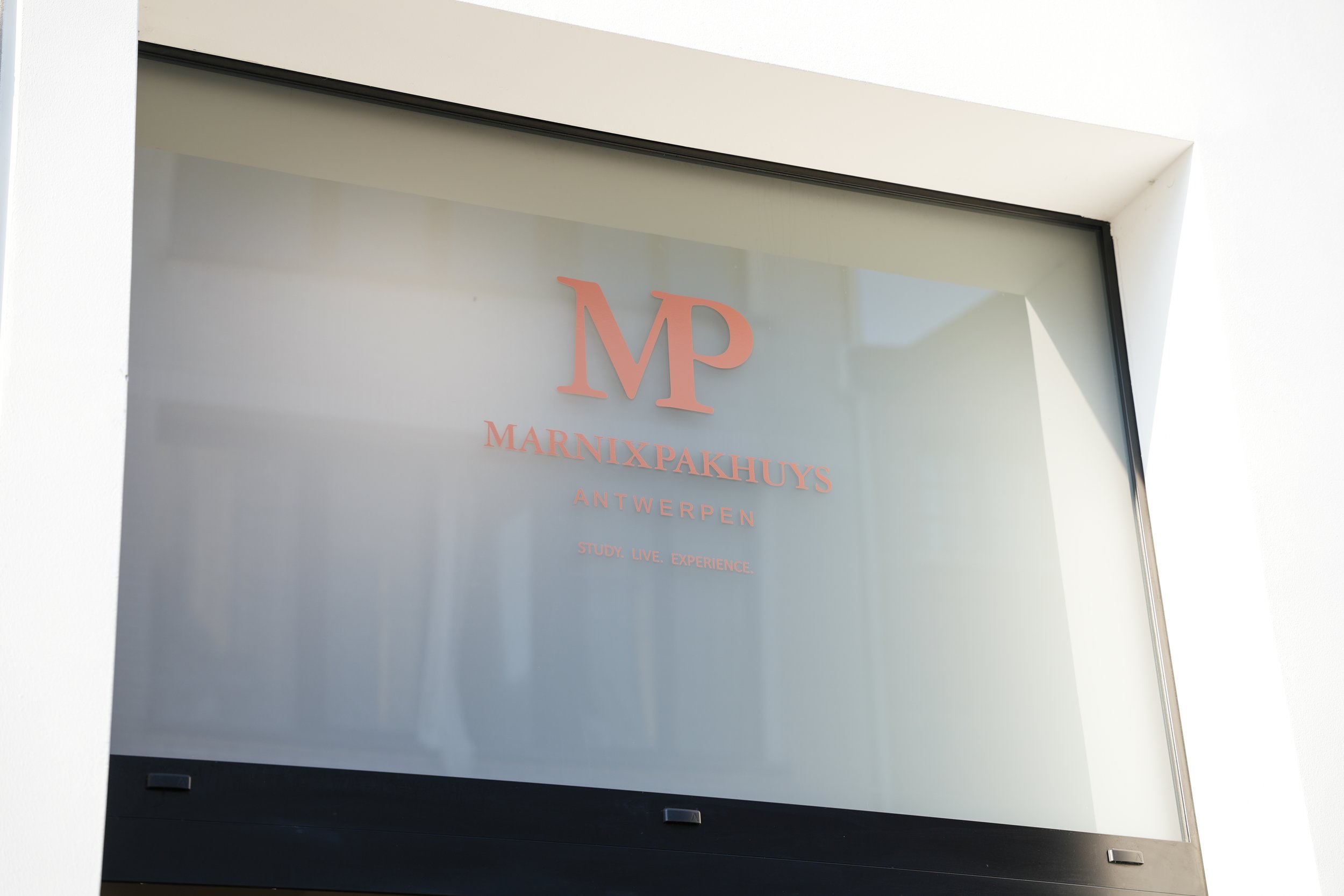 Et glasvæg met de tekst 'MARNIXPAKHUYS ANTWERPEN' en slogan 'STUDY. LIVE. EXPERIENCE.'