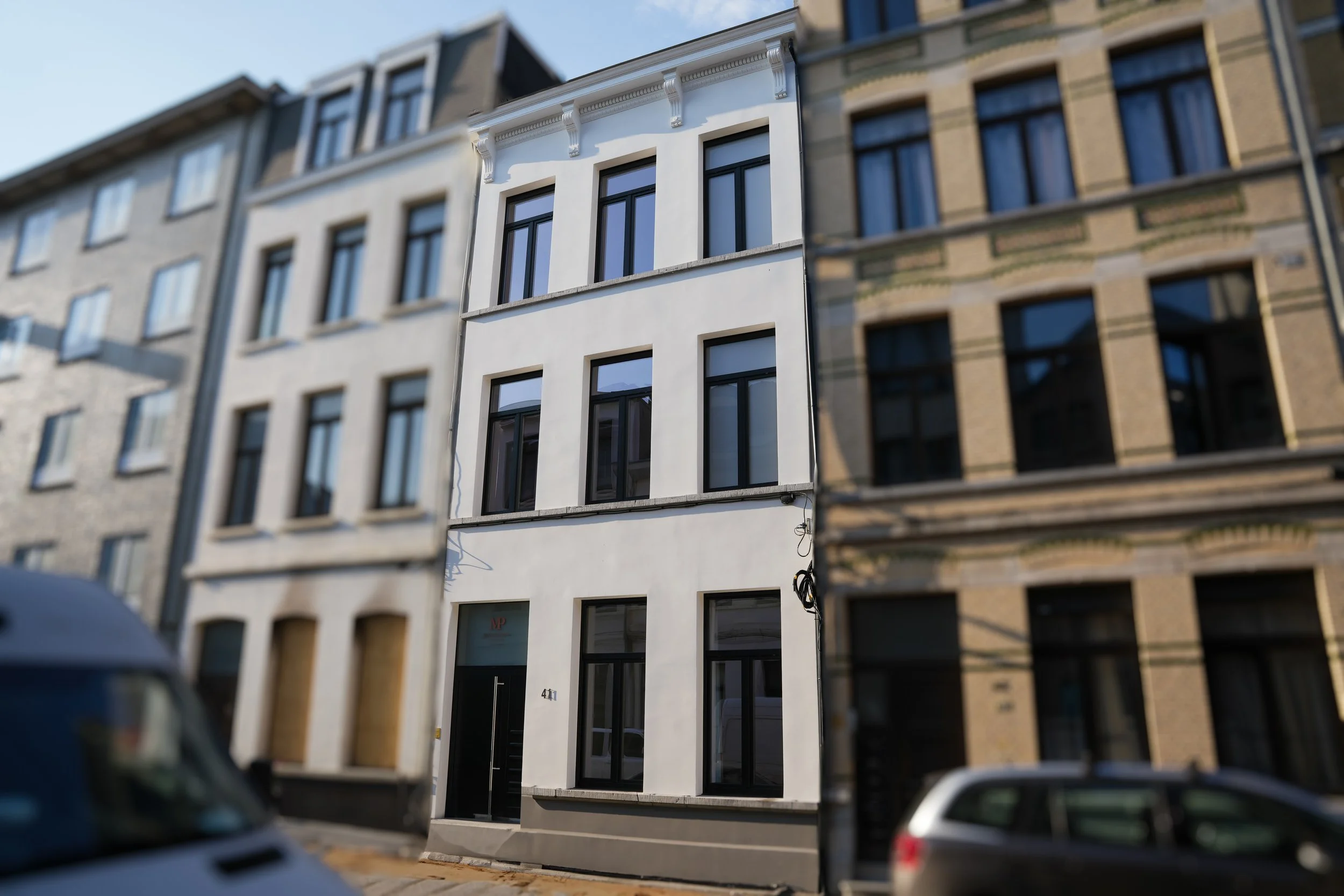 Modern witte gebouw met grote ramen en decoratieve geveldetails, straatzicht met auto en voetpad