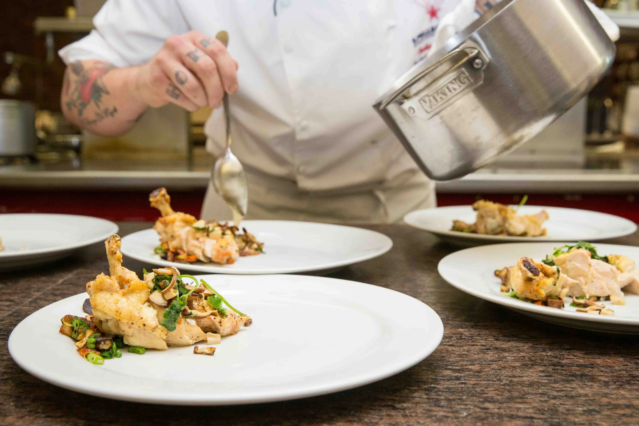 Chef garnishing plates with chicken and vegetables.