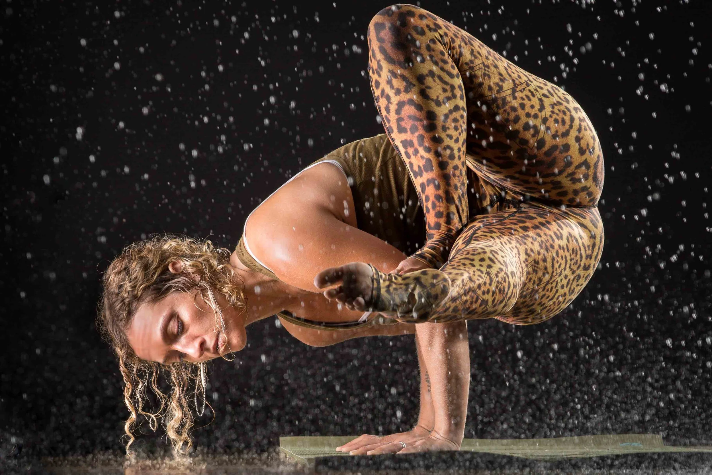 A woman in yoga attire performing a yoga pose on a mat with water splashing around her.