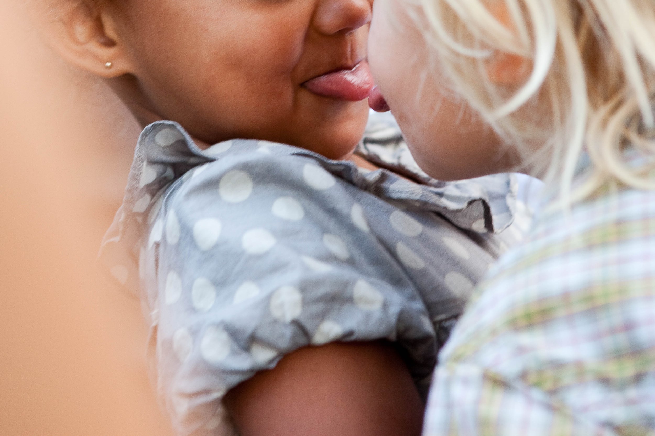 Close-up of two young children with their faces close together, showing only parts of their faces, one with blond hair and the other with darker hair, wearing casual clothing.
