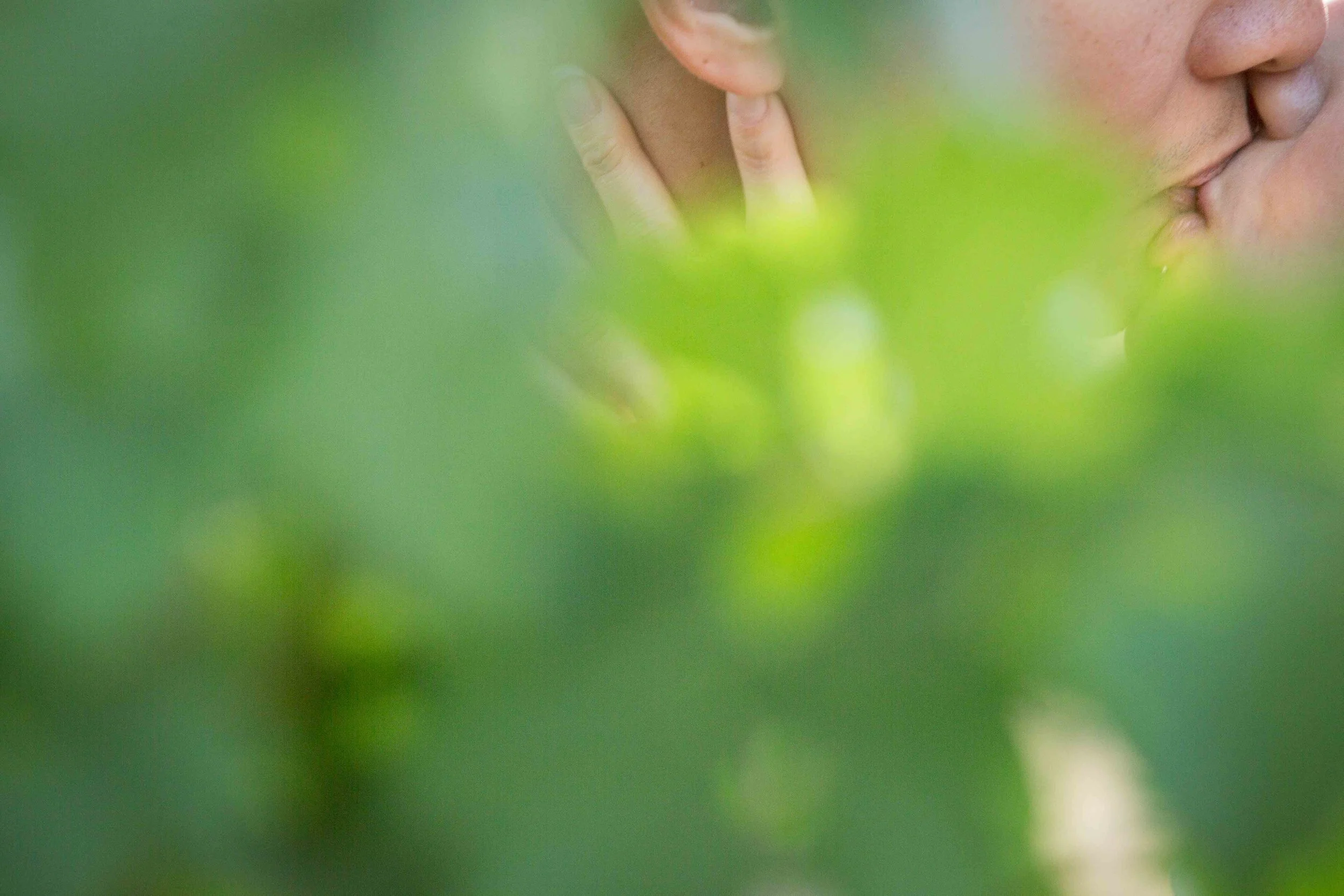 Close-up of a person's face and hand, with a finger near their ear and lips touching.