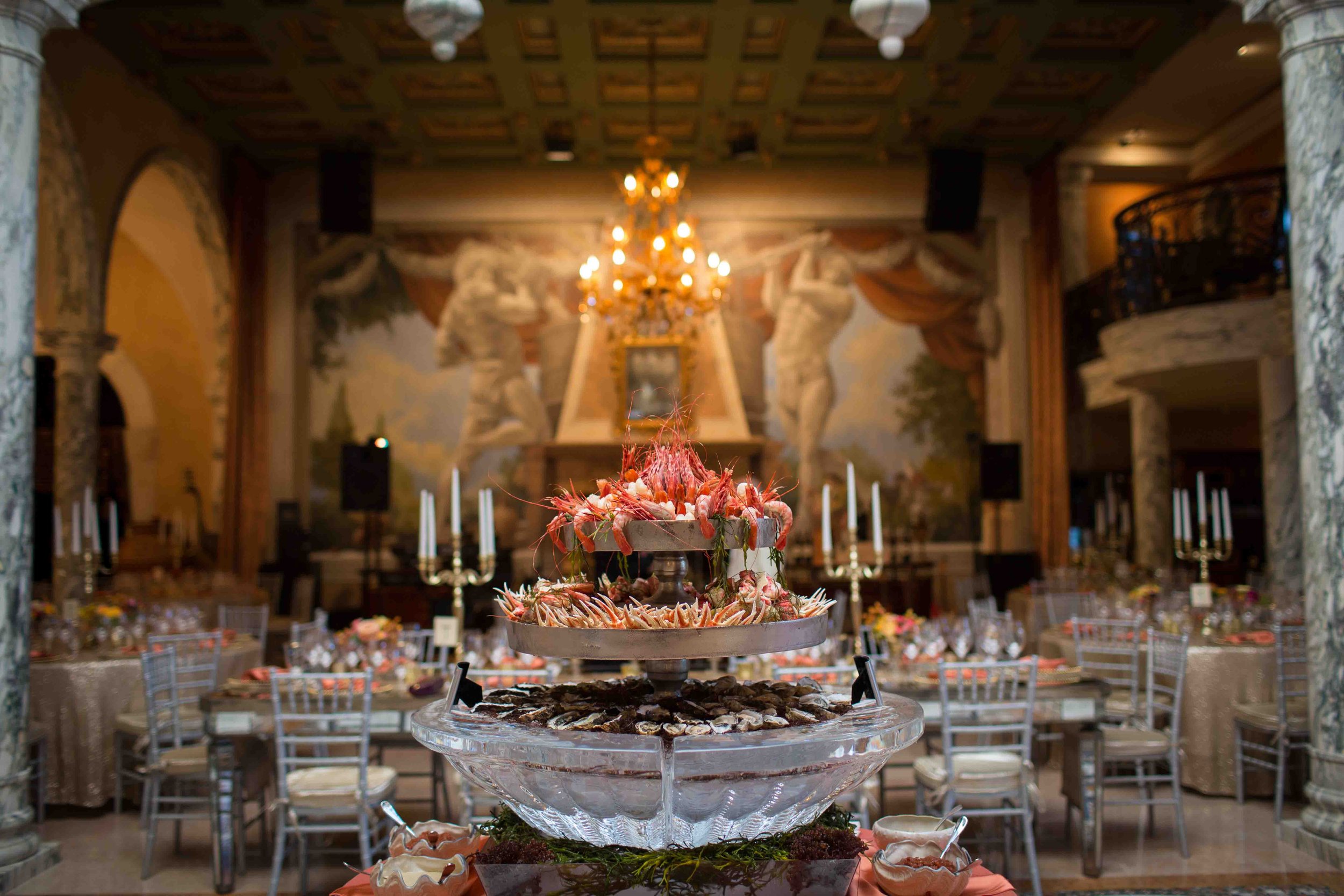 Seafood display with lobster and oysters on a tiered tray in an elegant grand banquet hall with chandeliers and candelabras.