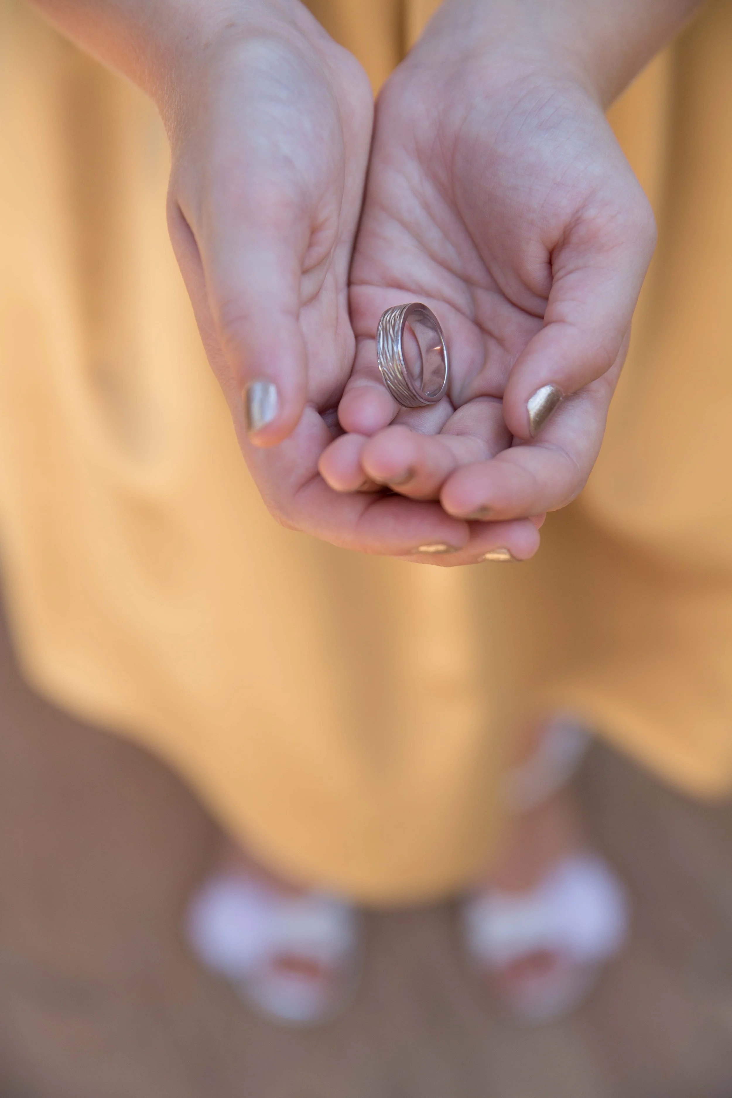 A person holding a silver ring with intricate design details in their hands, wearing a yellow dress.