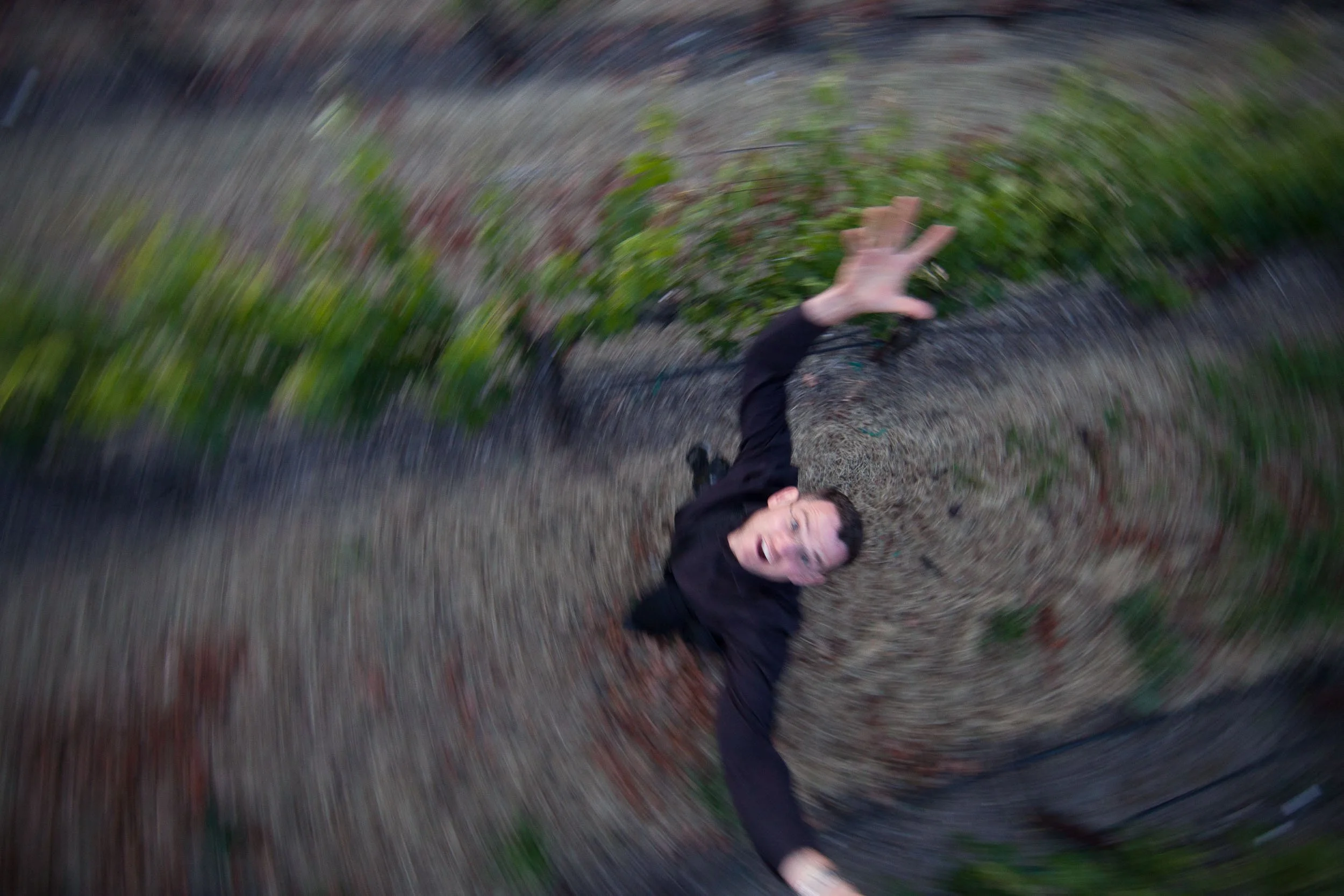 Person looking up with hand raised in an outdoor setting with green foliage, captured with a swirling motion effect.