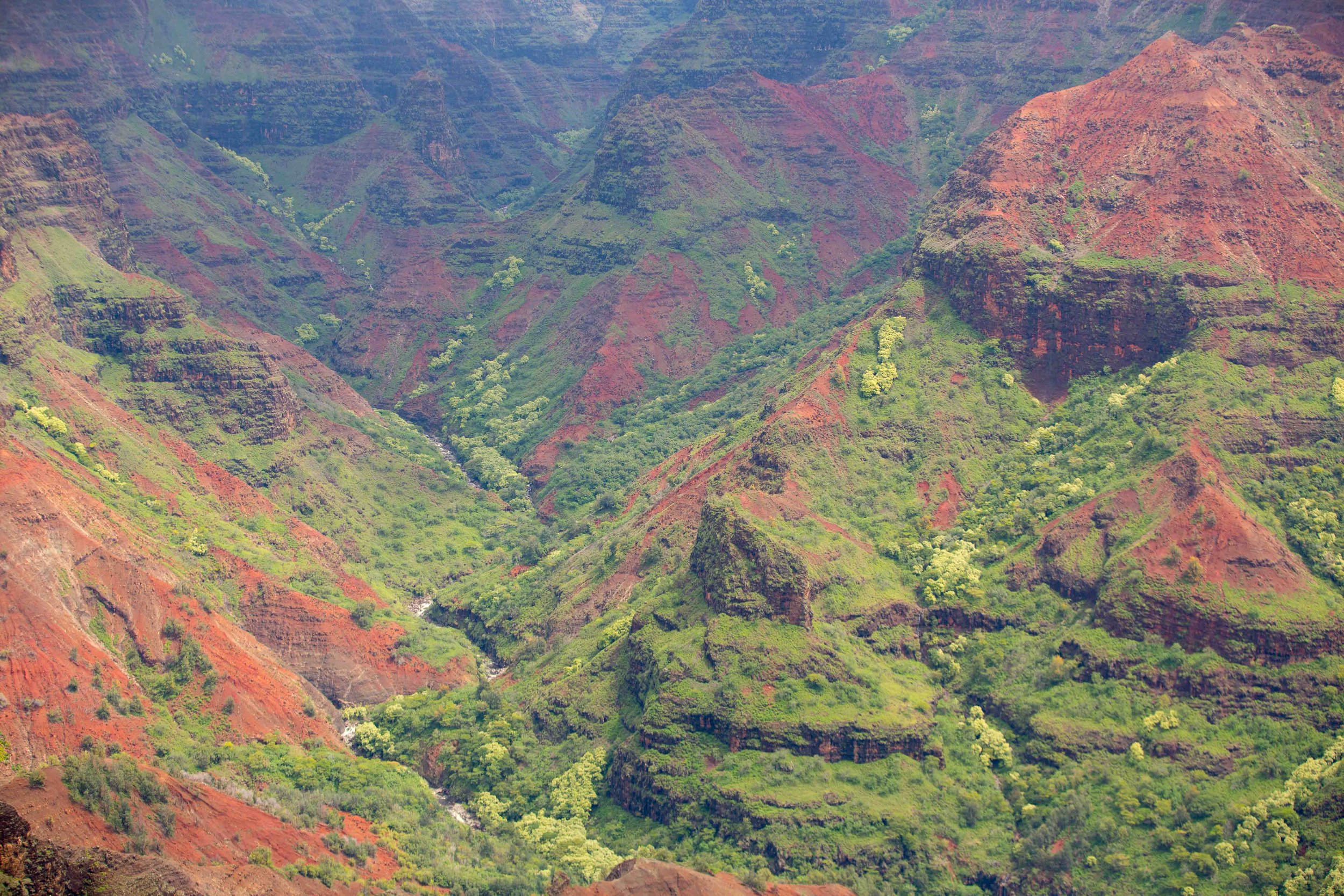 Aerial view of lush green and red volcanic mountains with a river running through the valley.