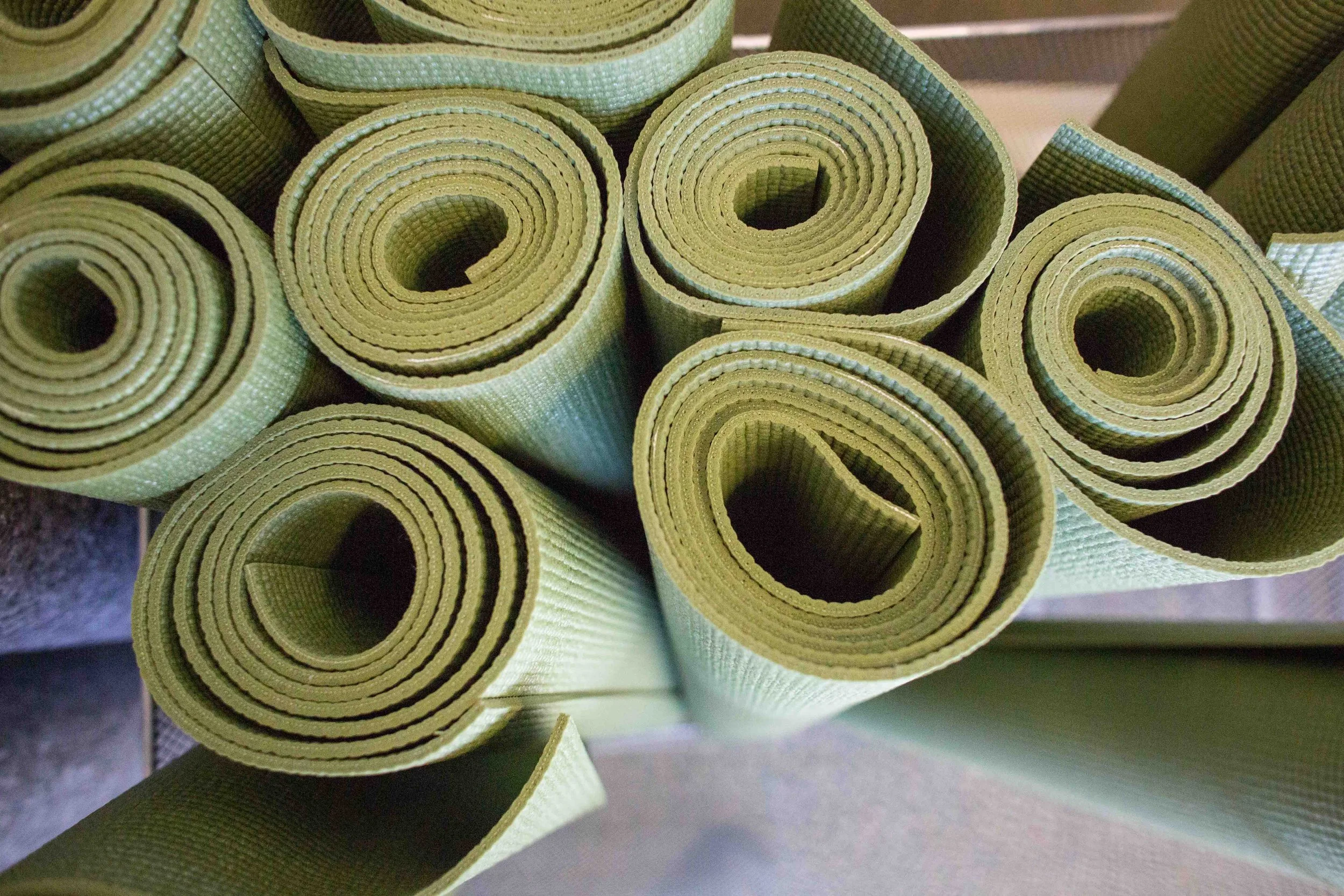 Multiple green rolled-up yoga mats arranged vertically.