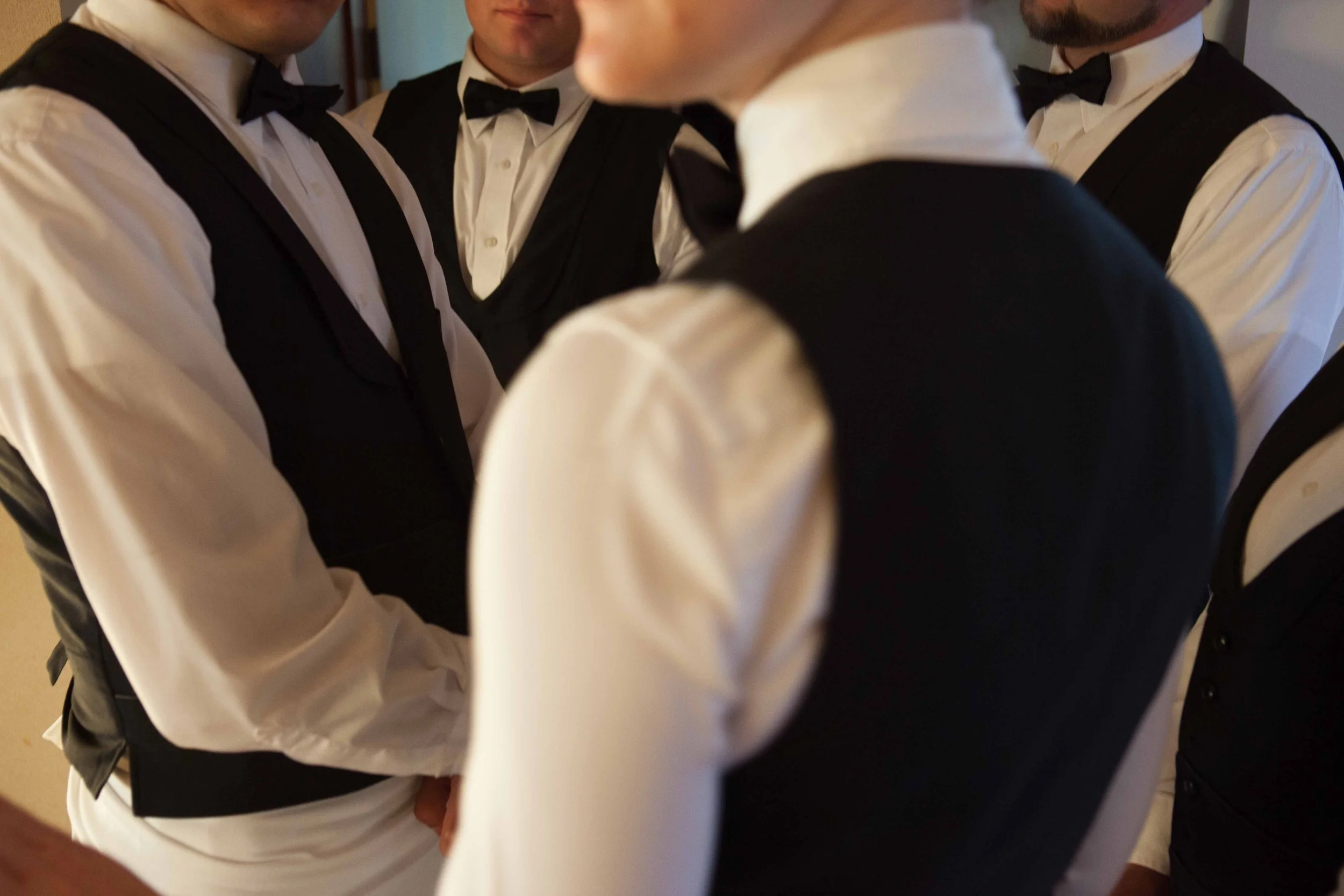 A group of men dressed in formal tuxedos and bow ties, standing close together, likely preparing for a formal event or wedding.