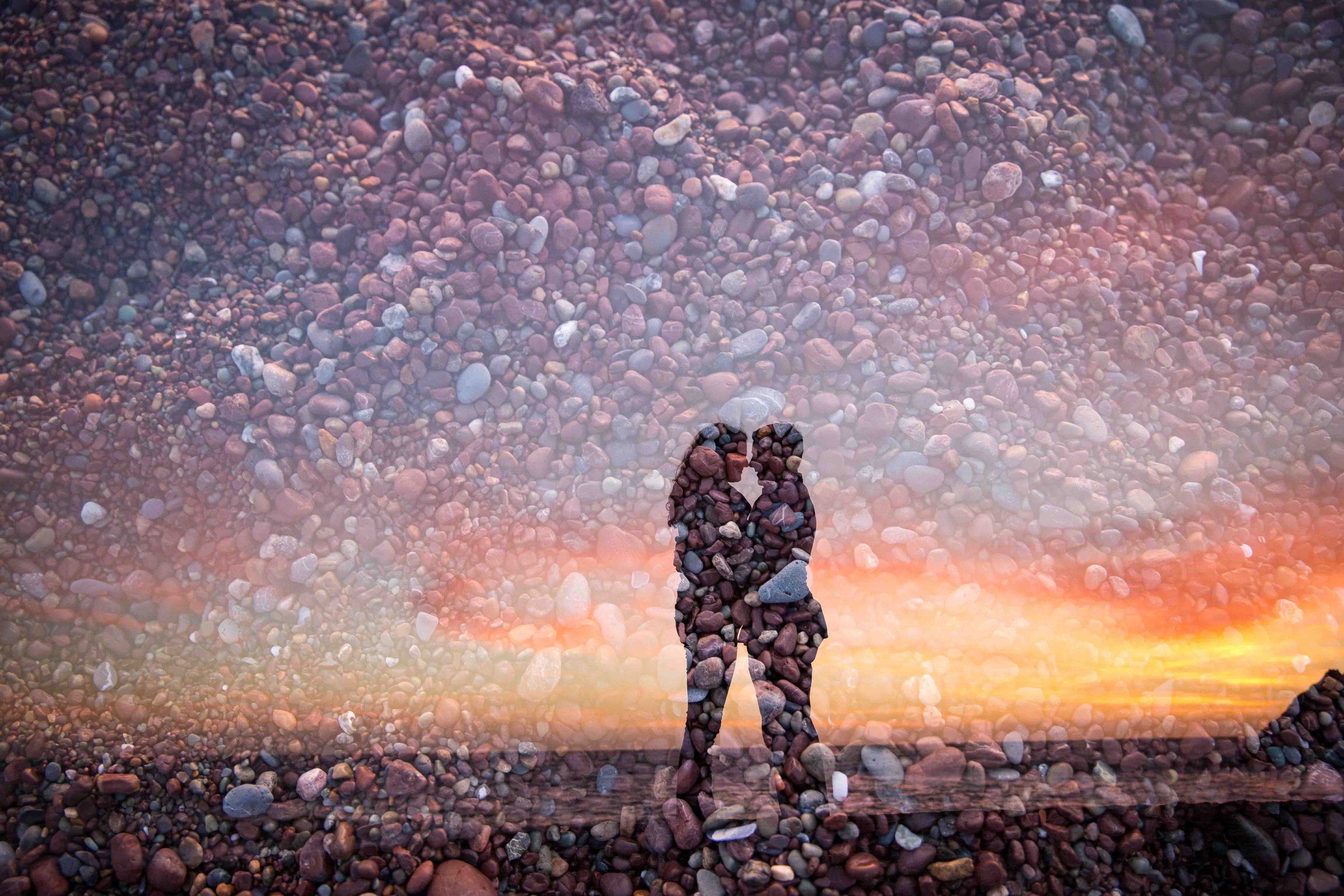 A couple's silhouette made of pebbles on a beach at sunset, with the couple kissing.