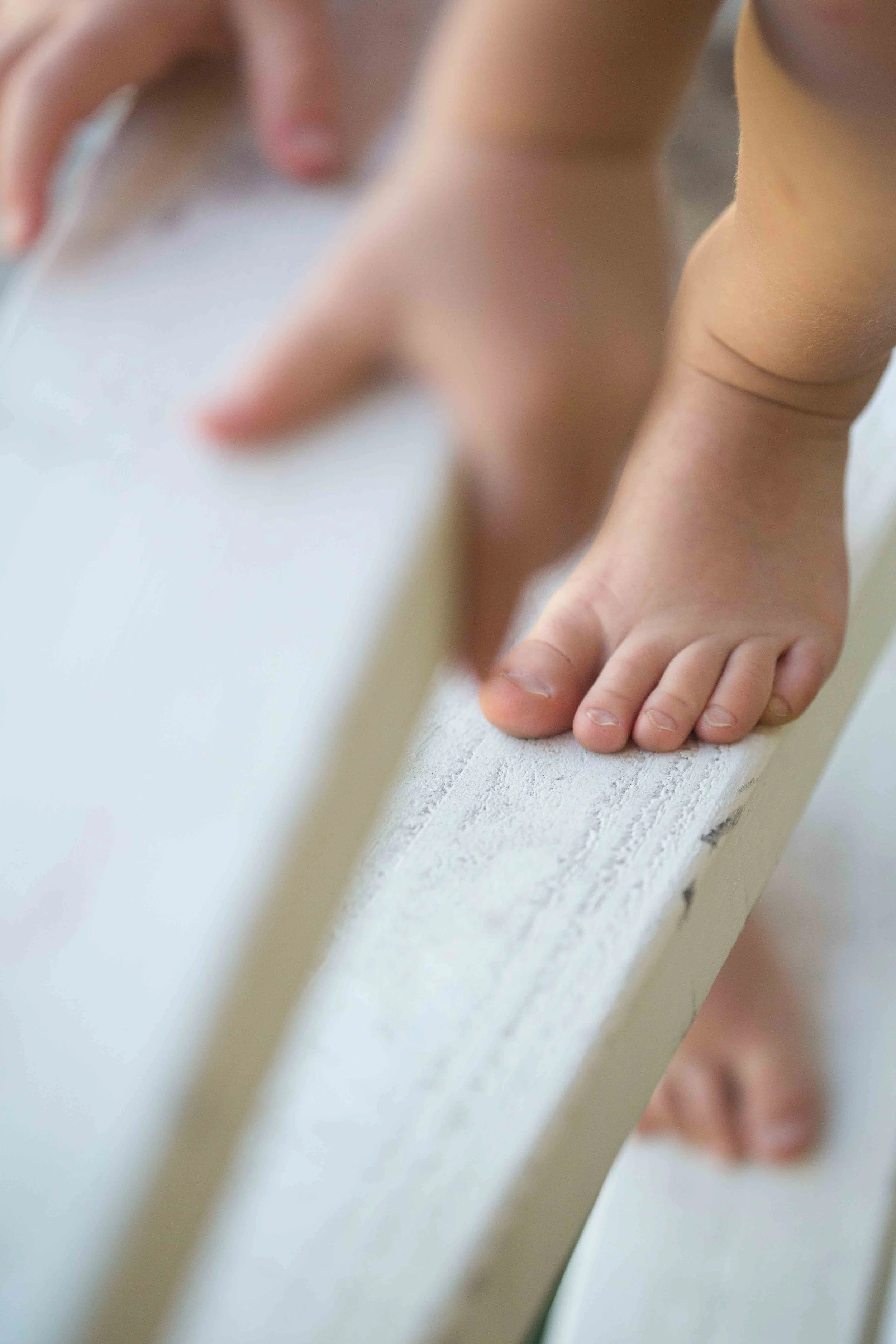 Close-up of a child's hand and foot on a white wooden surface, with a paintbrush in hand.