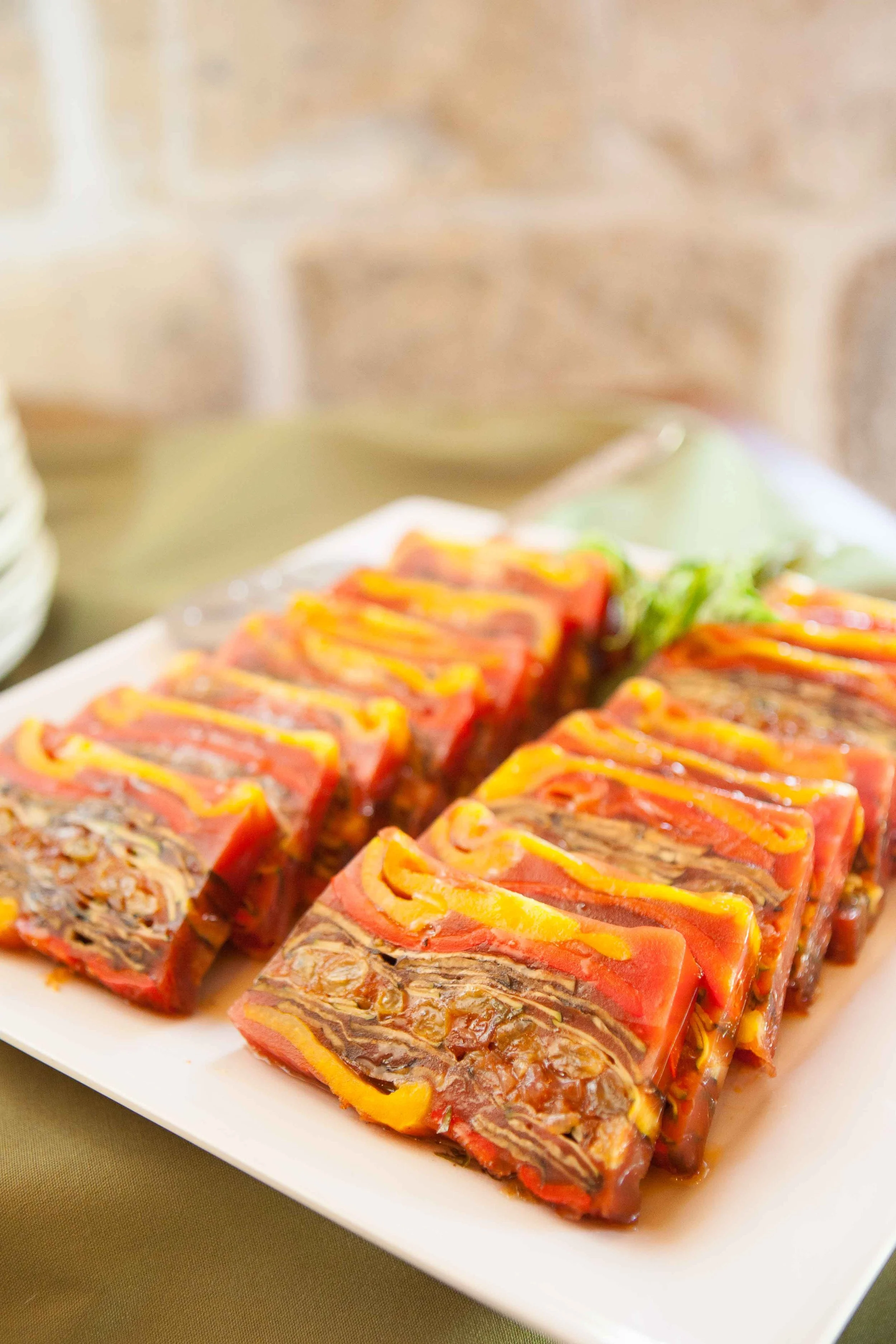 Slices of layered meat terrine with a yellow sauce drizzle on a white platter with a green background.