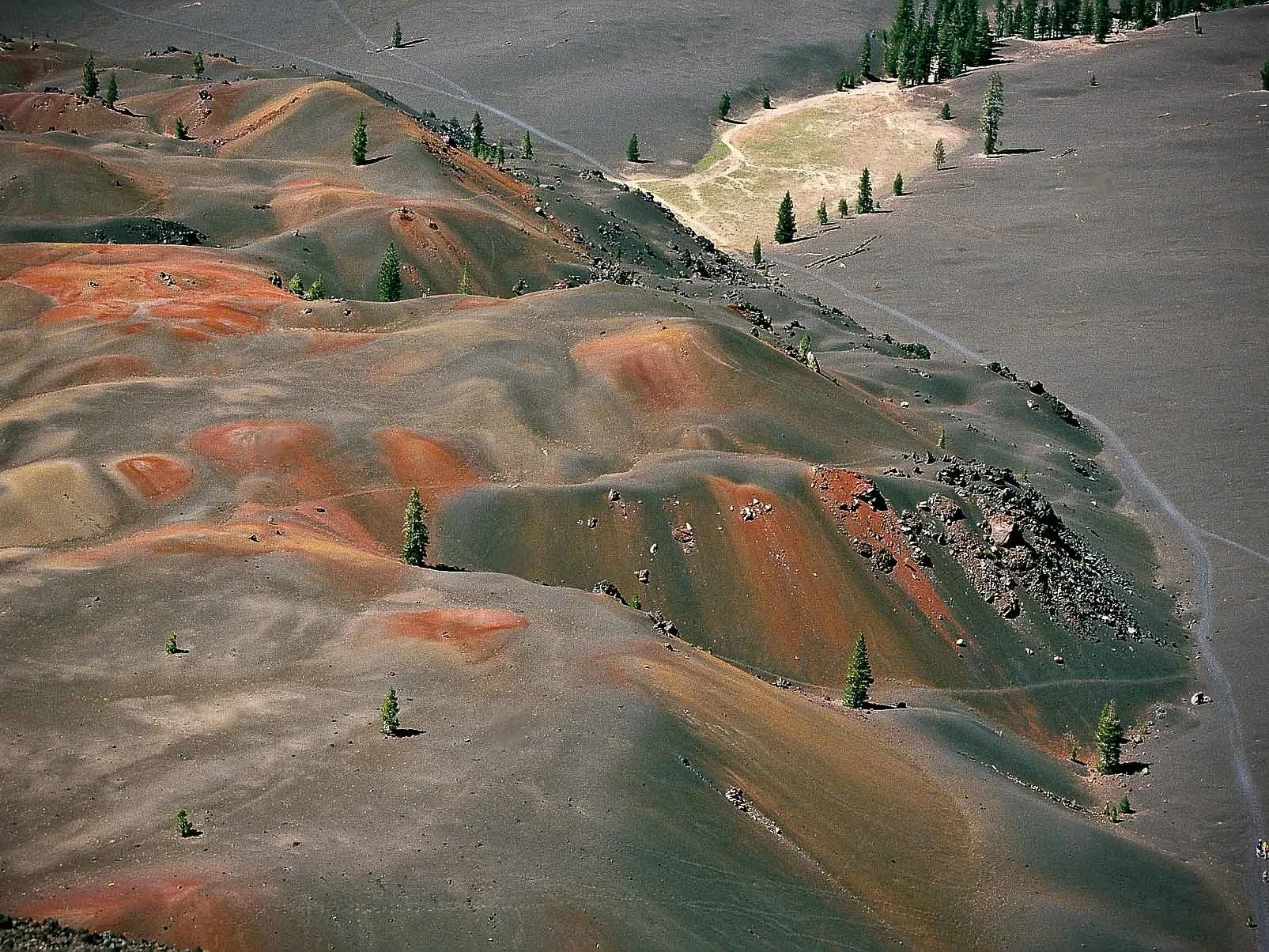 Aerial view of a colorful mountainous landscape with rolling hills and sparse trees.