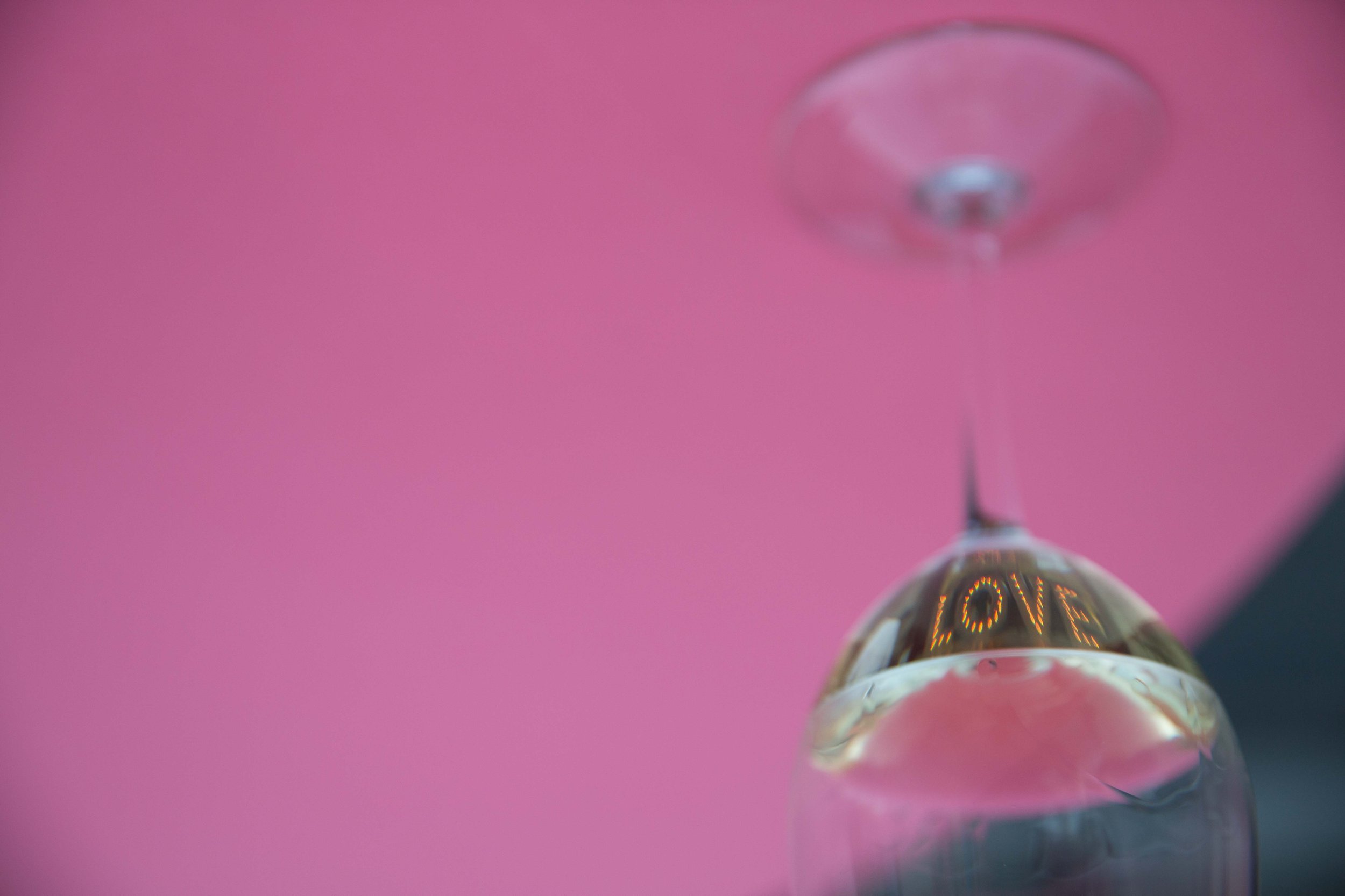 Close-up of a hanging glass ornament with the word 'LOVE' illuminated inside, against a pink background.