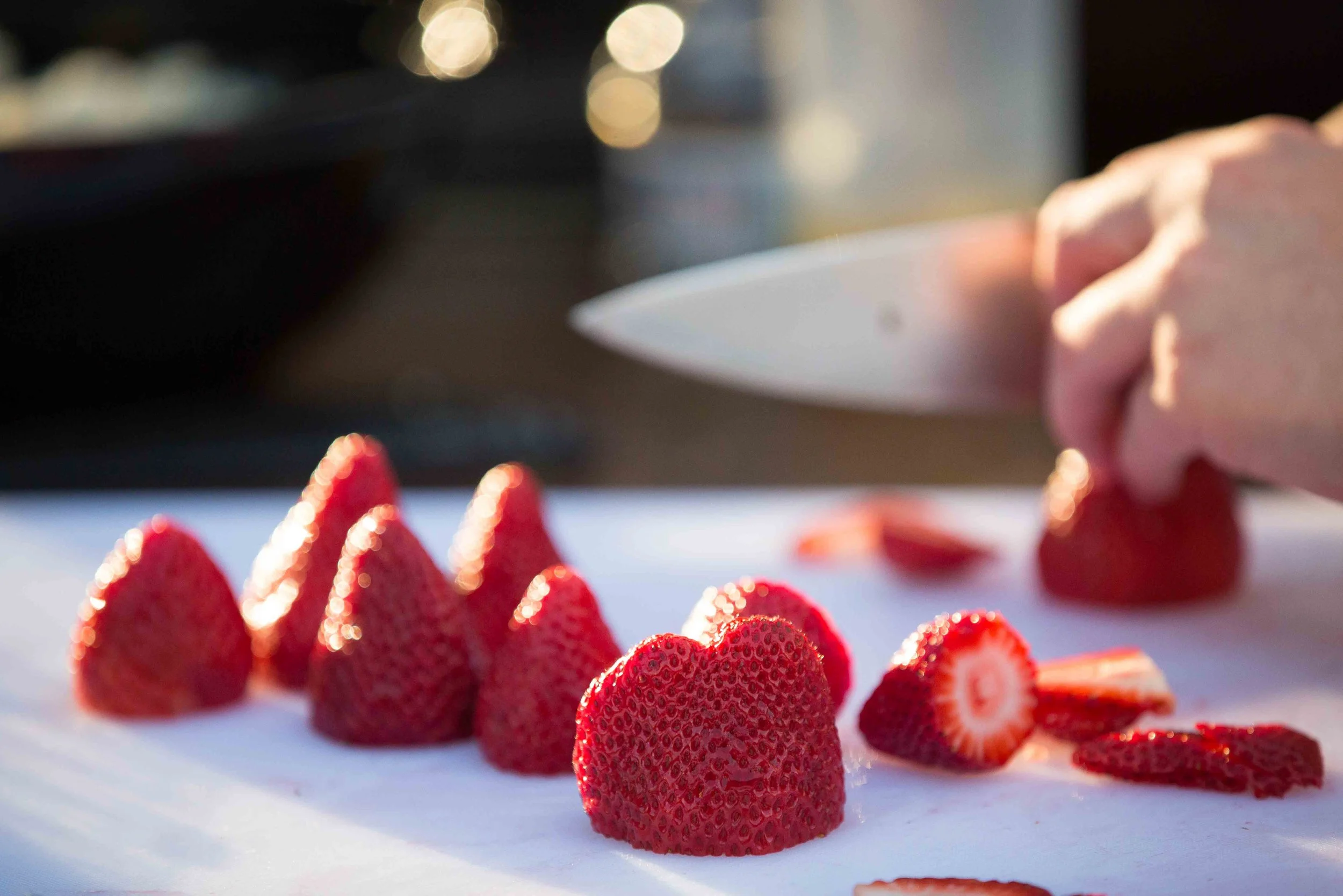 Close-up of fresh strawberries being sliced on a cutting board, with a person's hand holding a knife in the background.