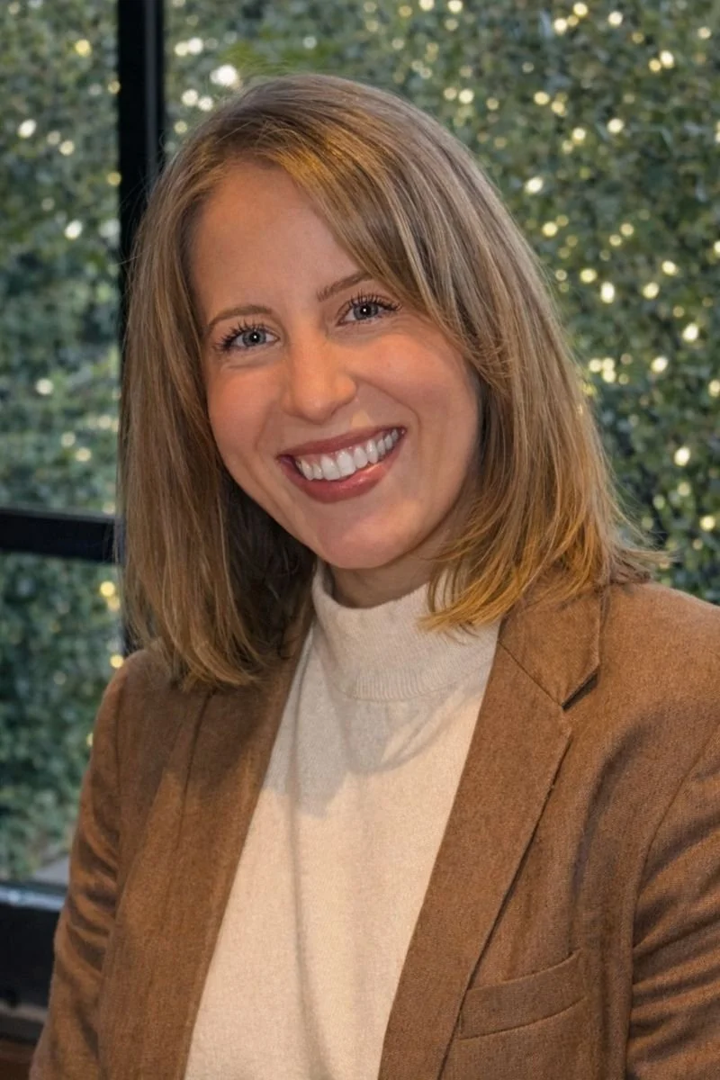 Portrait of Alex Yoss, licensed clinical social worker, smiling indoors with natural light and trees in the background.