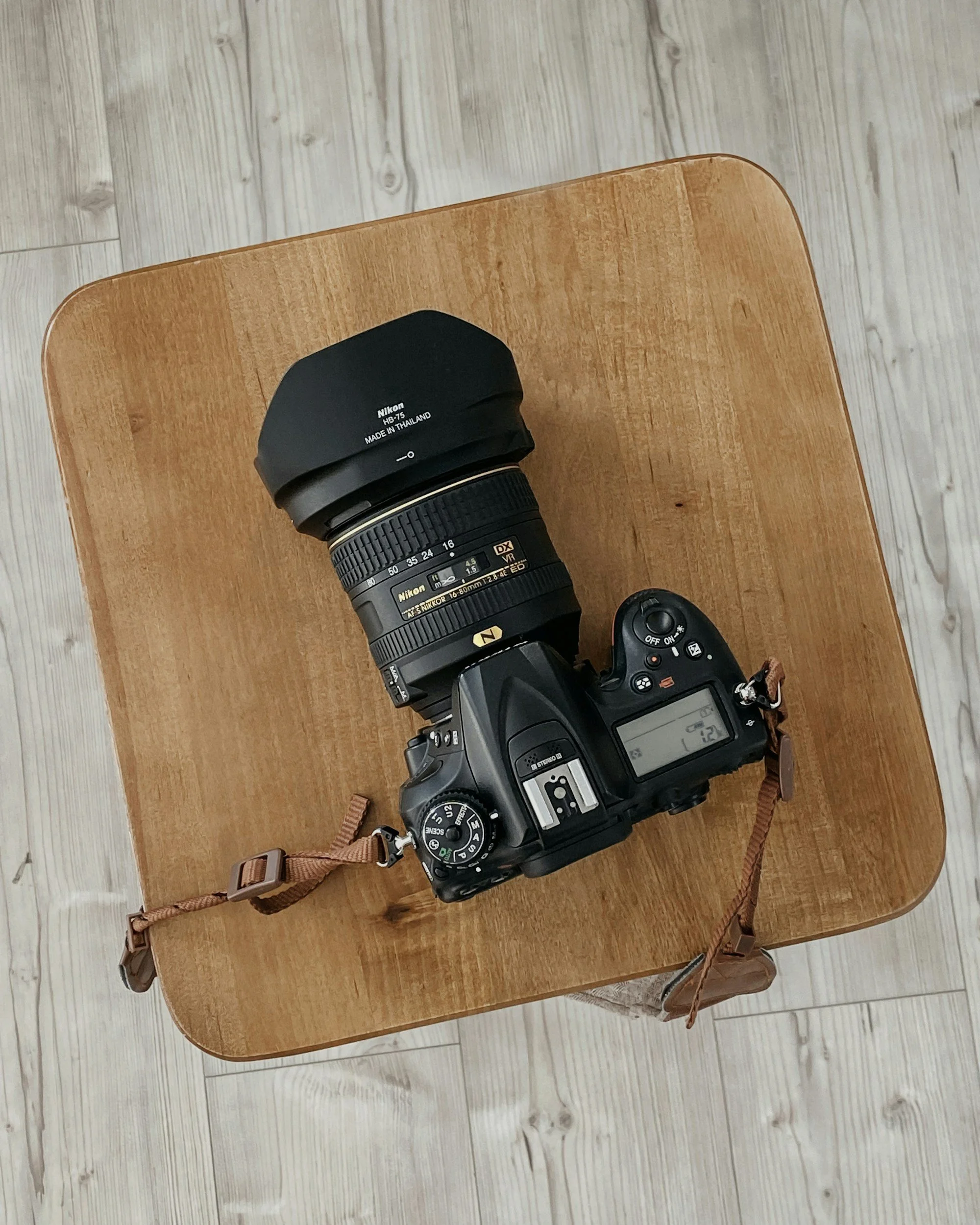 A Nikon DSLR camera with a zoom lens and lens hood resting on a wooden table.