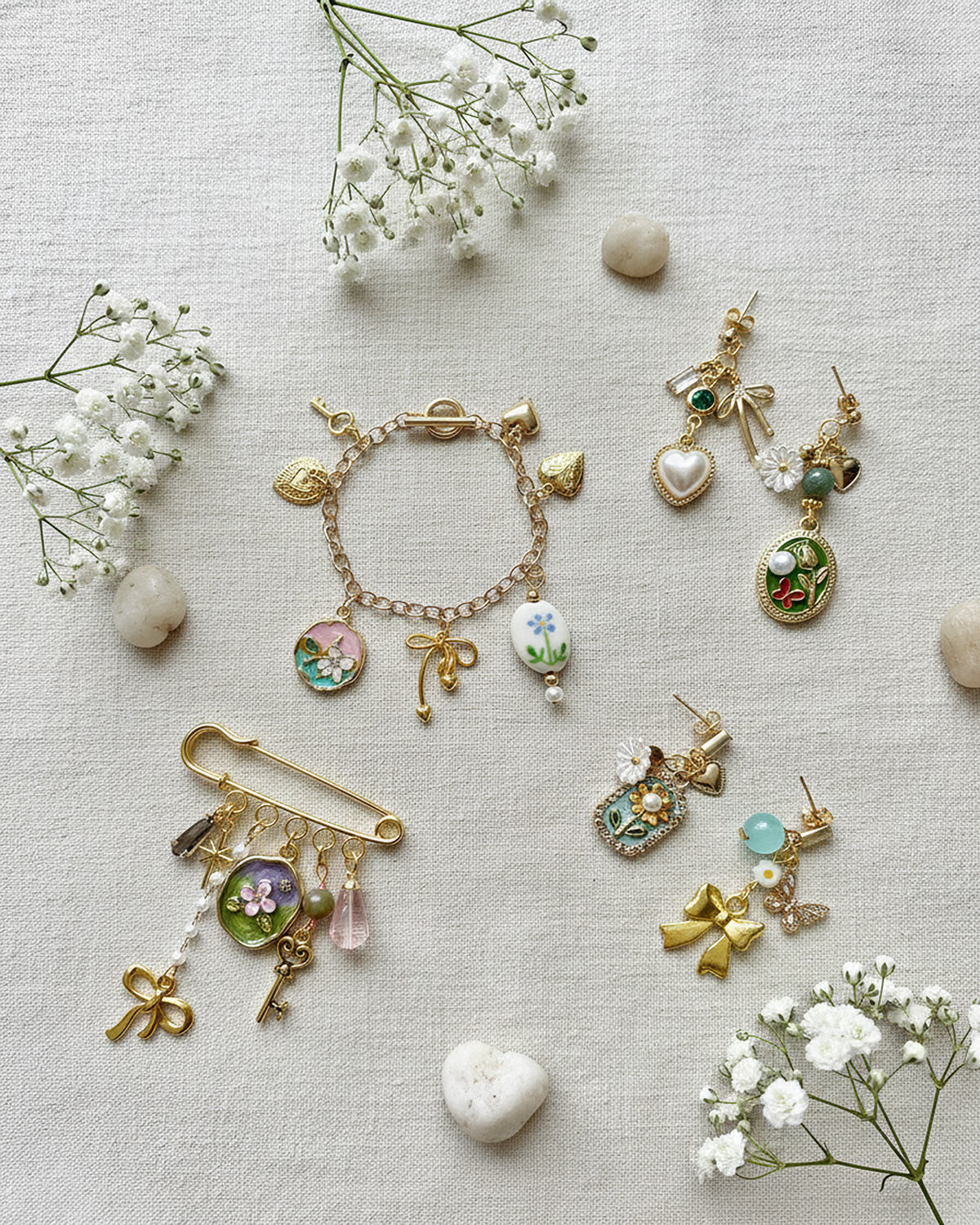 Collection of gold and silver jewelry, including bracelets and earrings with floral, bow, and nature-inspired designs, arranged on a light fabric surface with white flowers and small stones.