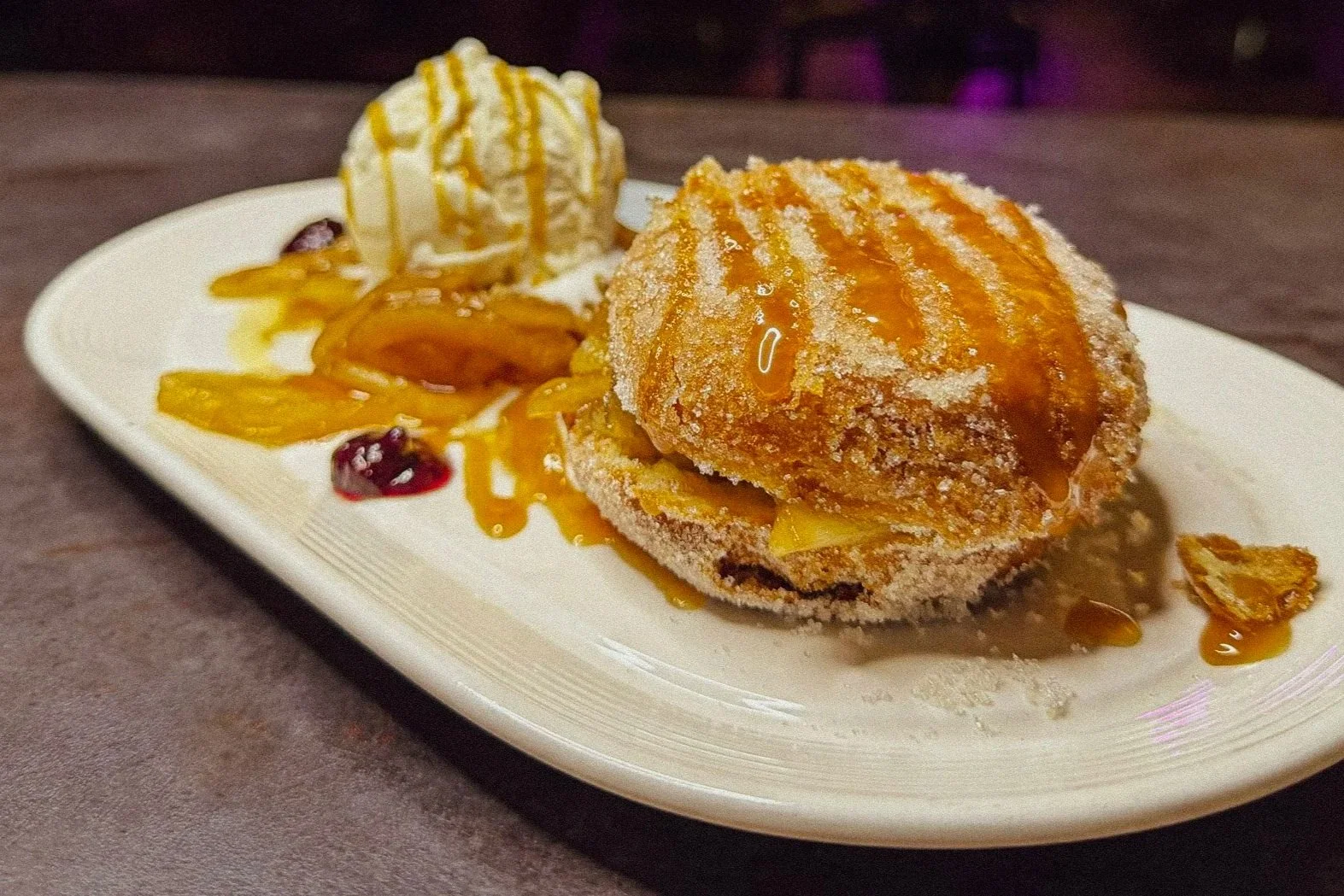 Fried dessert topped with caramel sauce, served with vanilla ice cream, caramelized apples, and a drizzle of caramel sauce on a white oval plate.