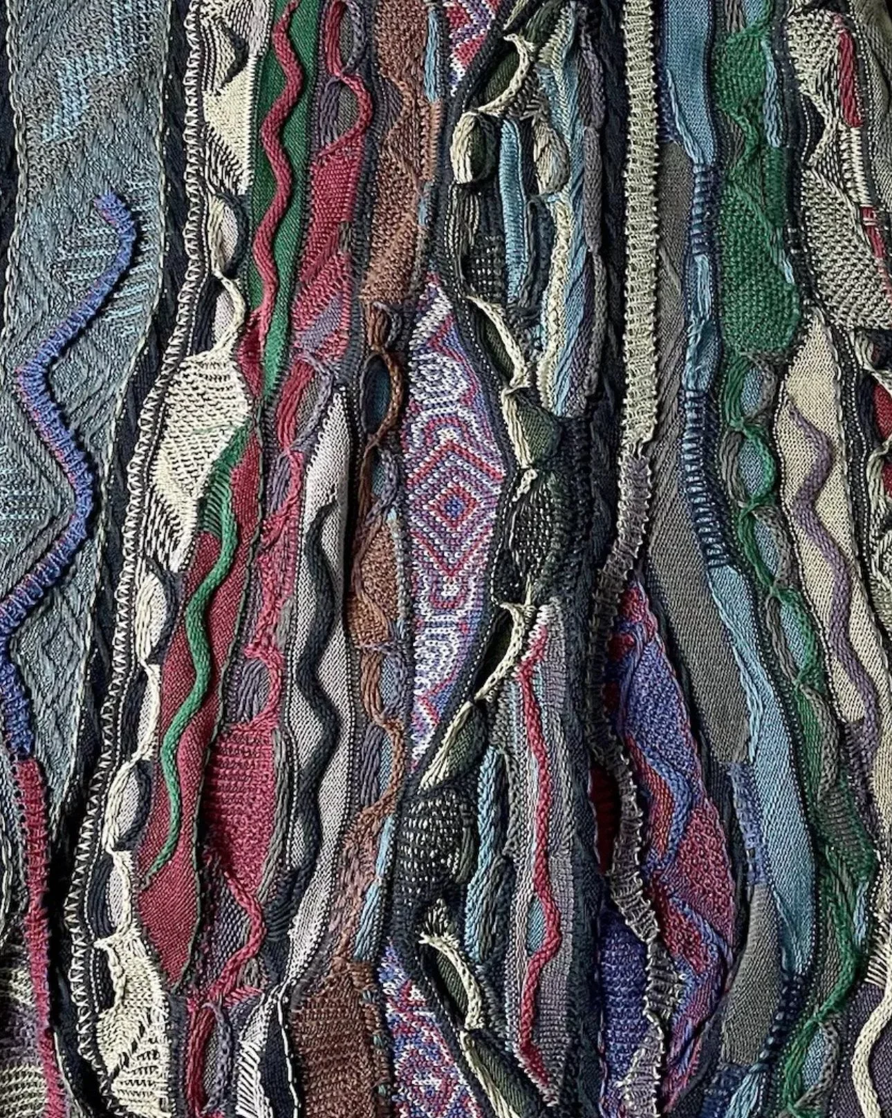 Close-up of a colorful, textured, woven fabric with various patterns and colors, including black, white, red, green, blue, and purple.