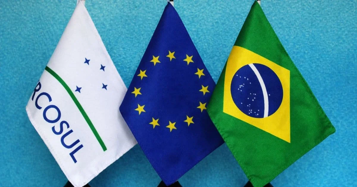 Bandeiras do Brasil, da União Europeia e de Pernambuco exibidas juntas contra fundo azul.