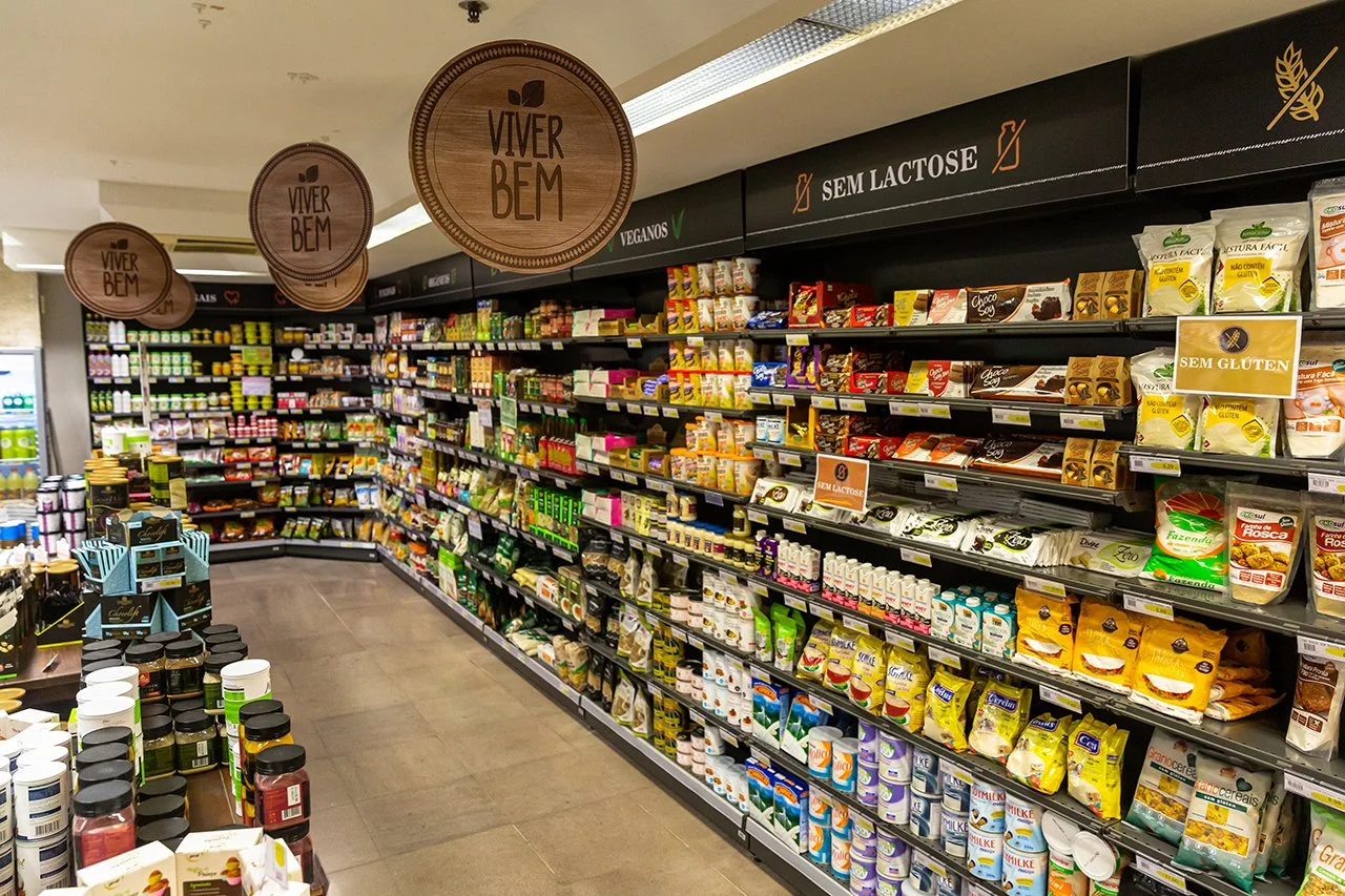 Prateleiras de supermercado com produtos veganos, sem lactose e sem glúten, com sinalização indicando cada categoria.