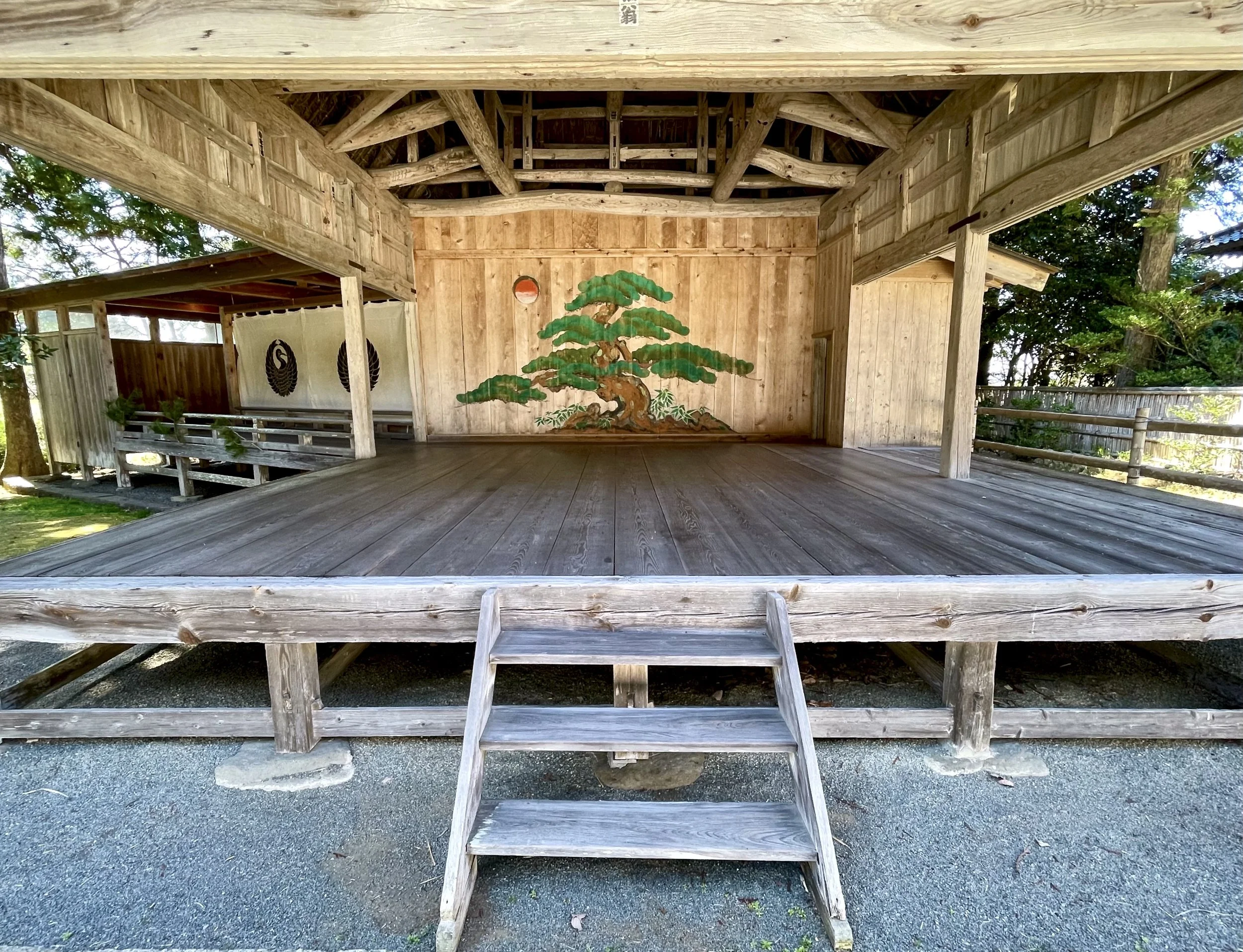 Wide view of a traditional Noh stage with painted pine tree and sun on the back panel