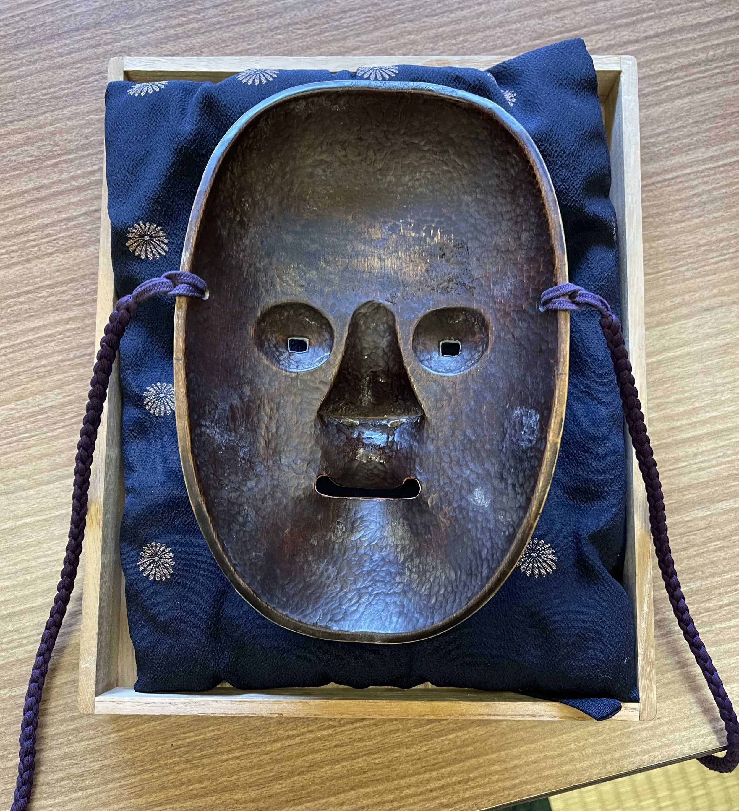 Interior of a traditional Japanese Noh mask showing the rough-hewn carved wood, eye openings, and attachment holes for the cords