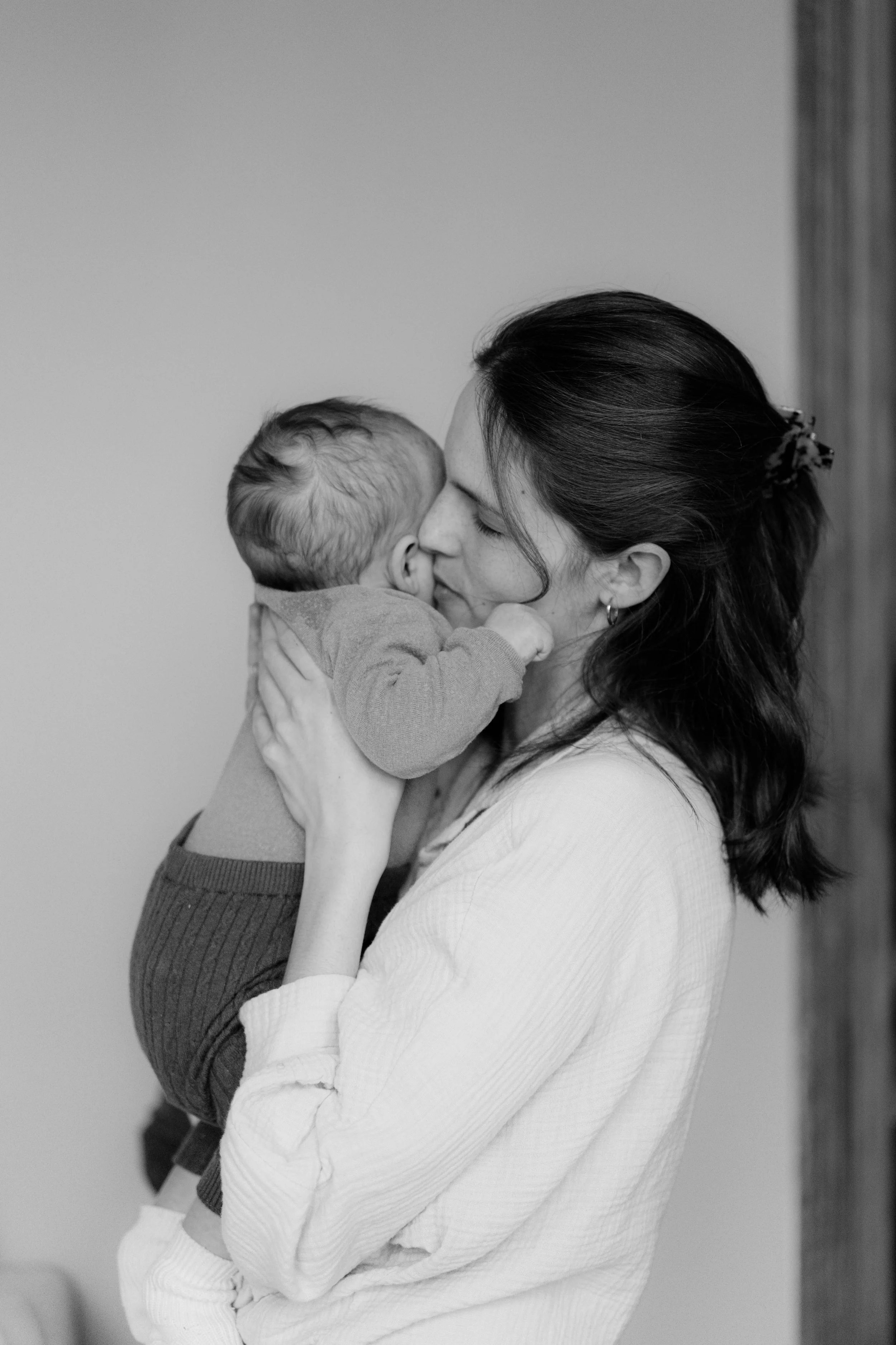 Eine Frau hält ein Baby im Arm, küsst es liebevoll. Schwarz-weiß-Foto, innige Momentaufnahme.