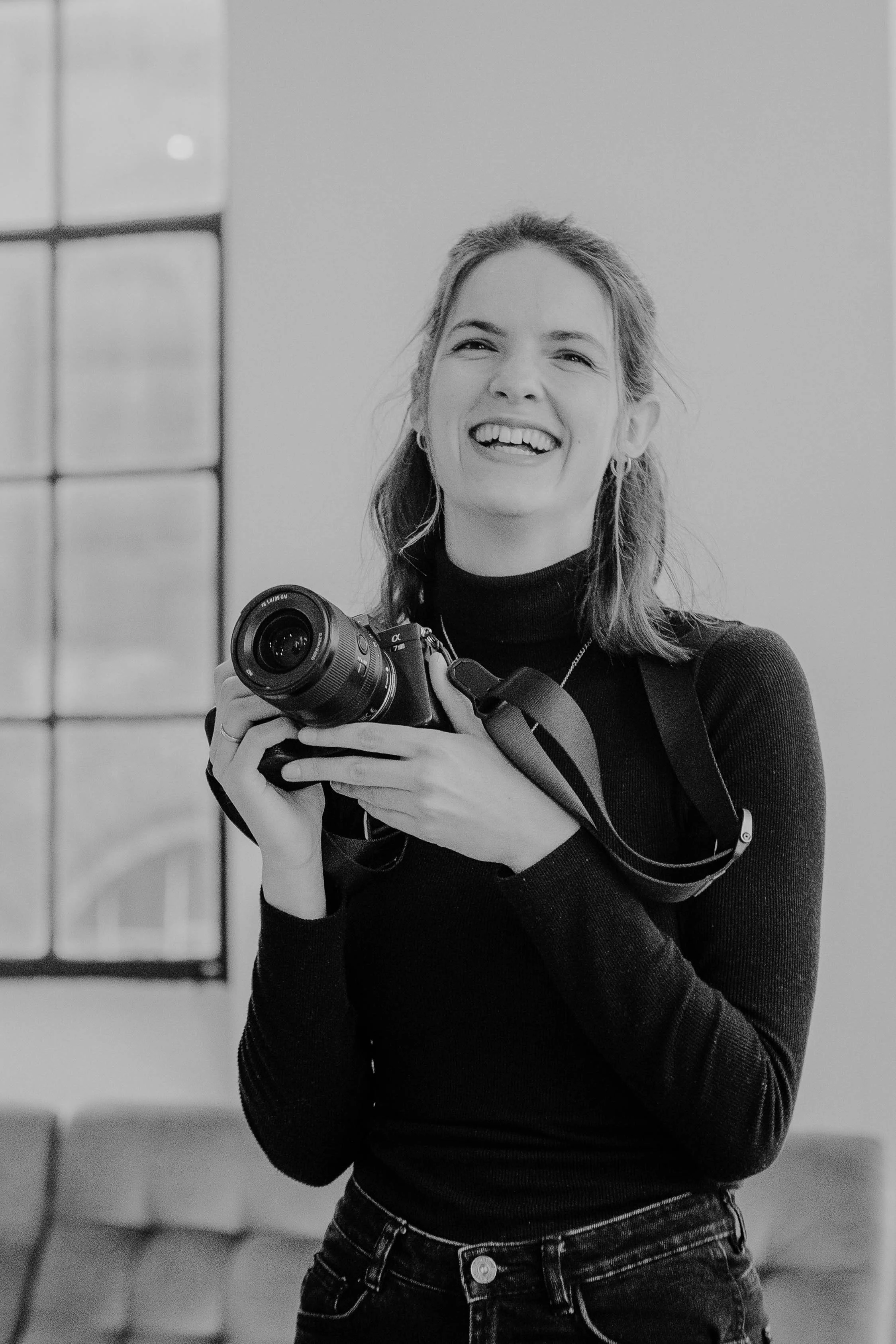 Lächelnde junge Frau mit Kamera, schwarz-weiß Foto, moderne Innenraumgestaltung.