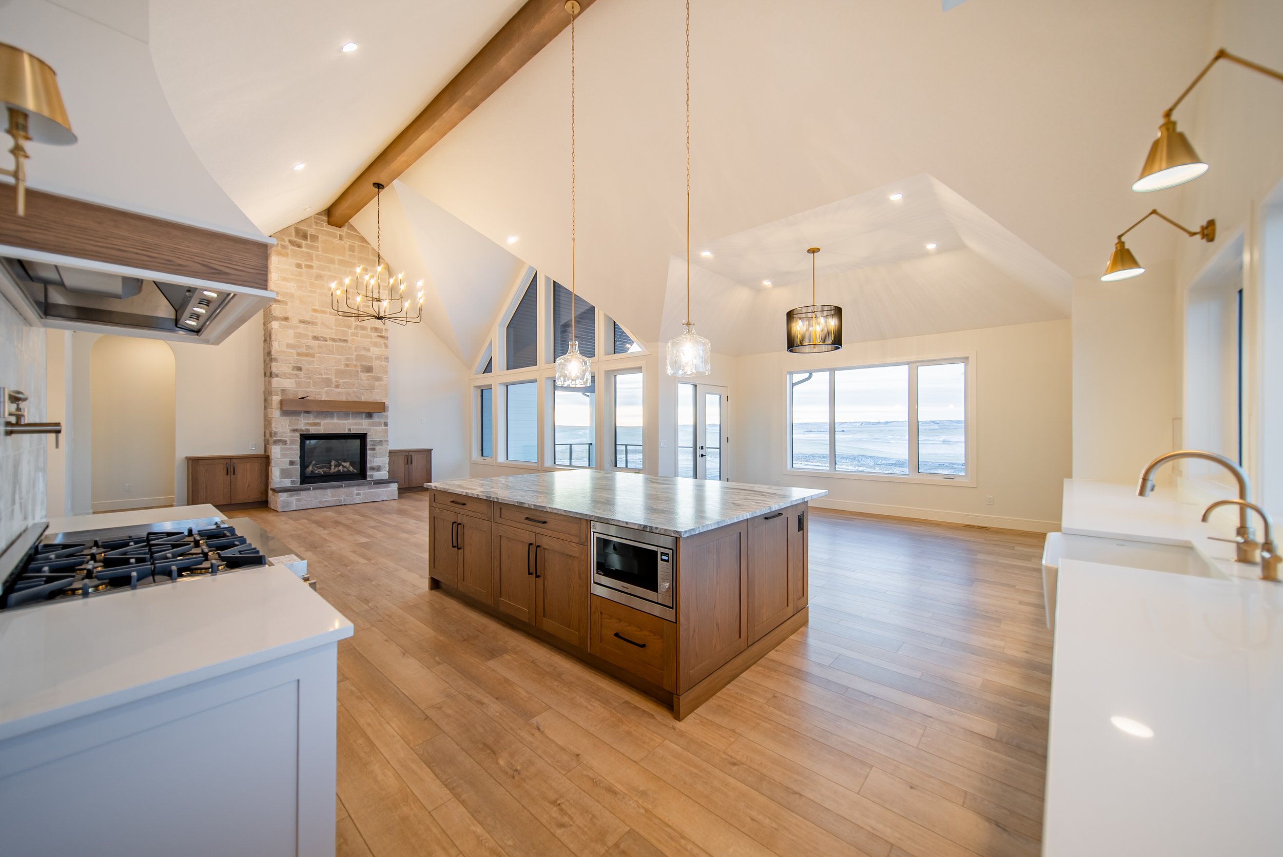 Open-concept kitchen and living room with wooden flooring, large windows, a fireplace, and a kitchen island with pendant lighting.