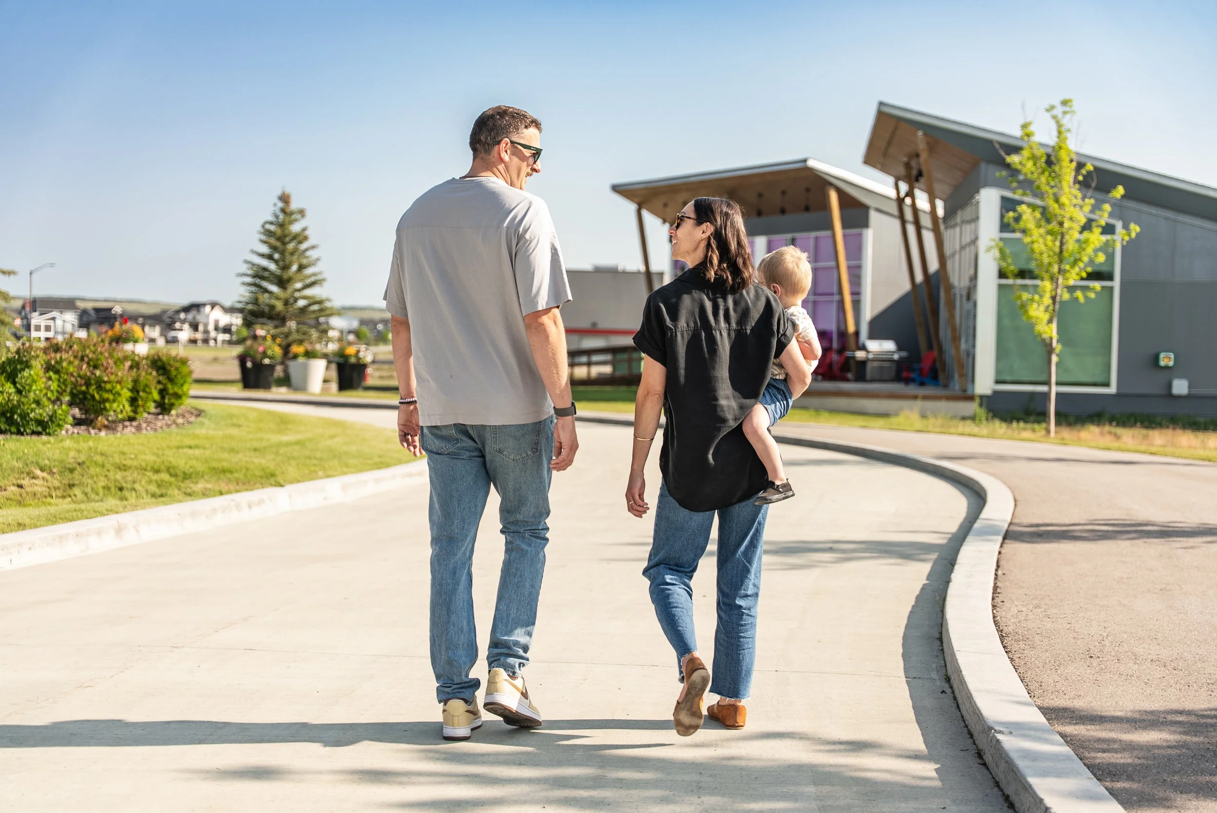 A family of three walking outside on a sunny day. The man and woman are walking side by side, with the woman carrying a small child in her arms.