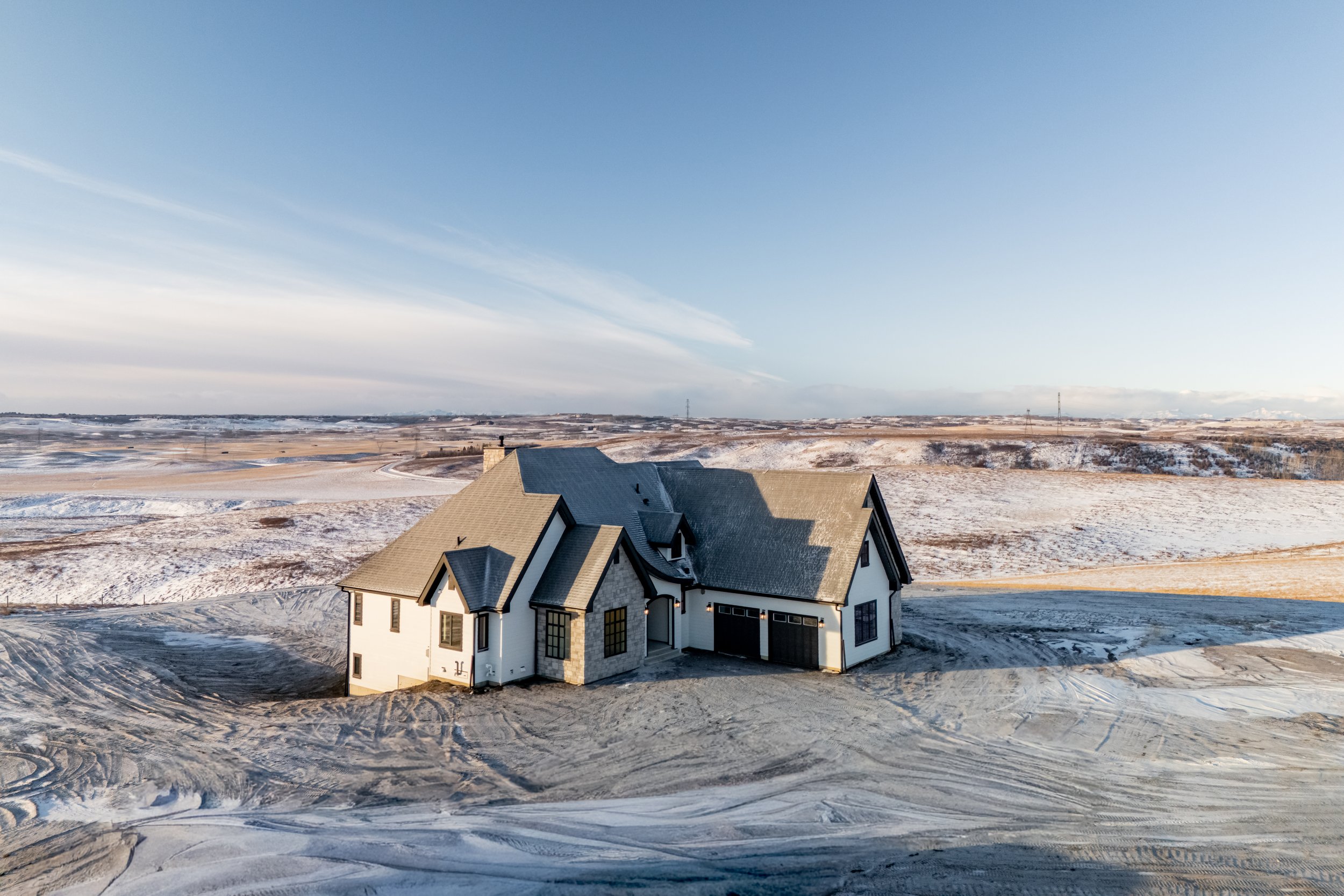 A large white house with a gray roof in a snowy rural landscape under a clear sky.