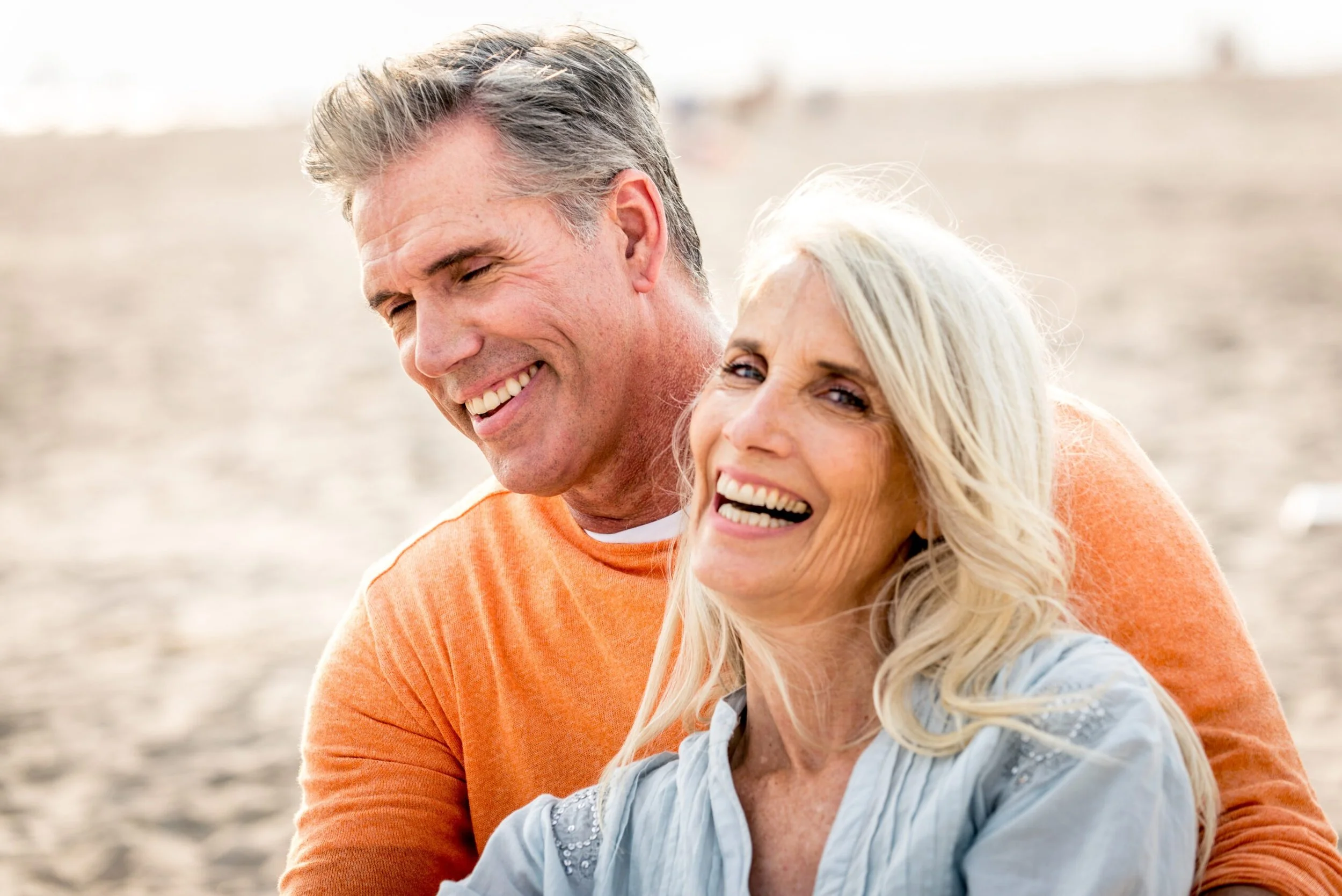 Smiling elderly couple on a beach, close-up of faces, cheerful mood, sunlight, casual clothing.