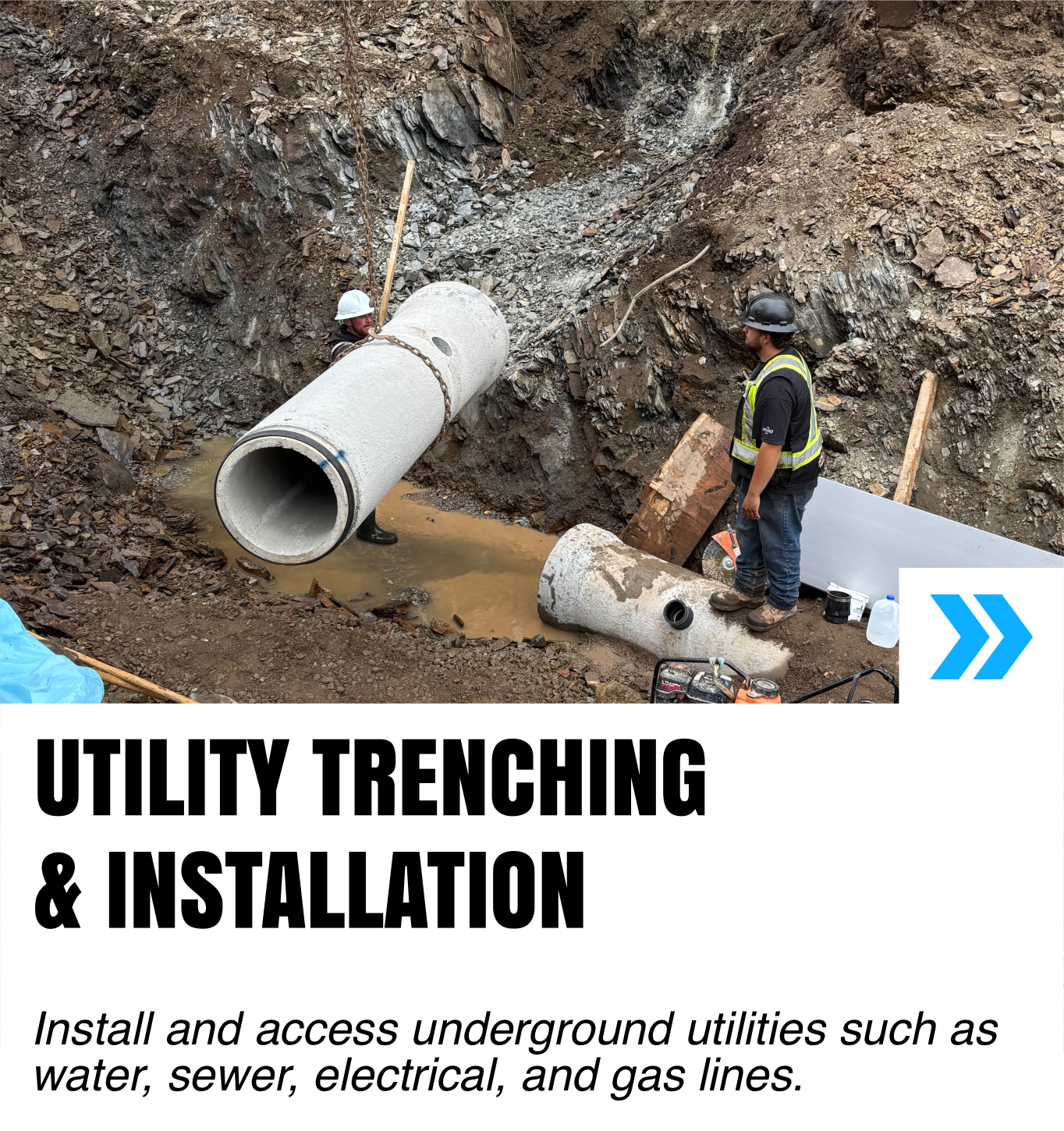 Workers installing large underground utility pipes at a construction site with a trench and muddy water.