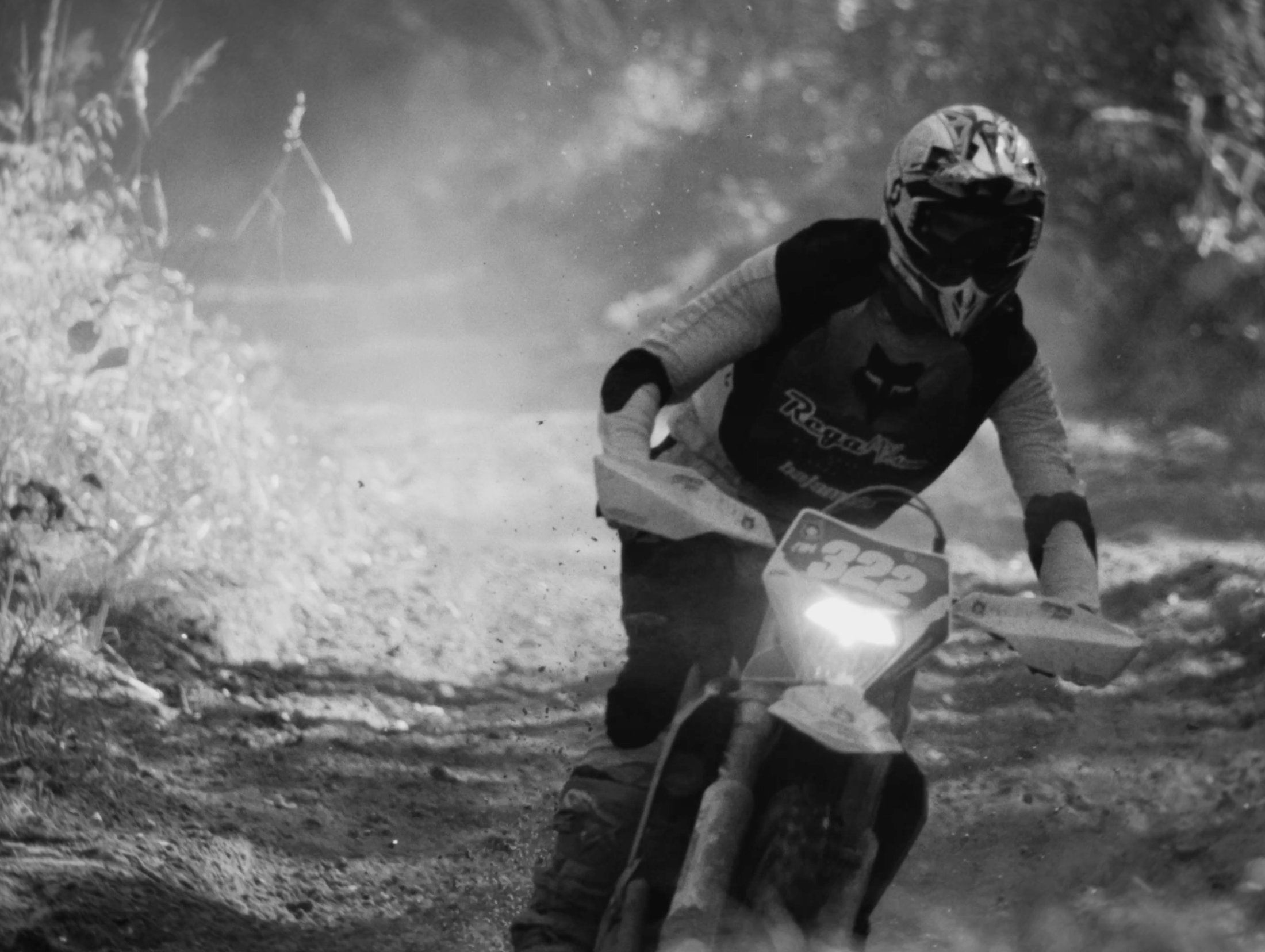 A person riding a dirt bike on a rugged trail, wearing a helmet and protective gear, kicking up dust.
