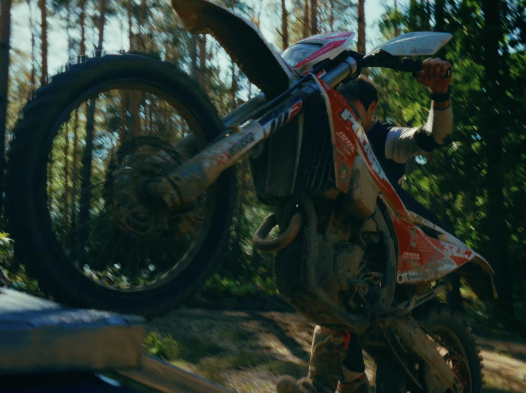 A motocross rider performing a wheelie stunt on a dirt trail surrounded by trees during daytime.