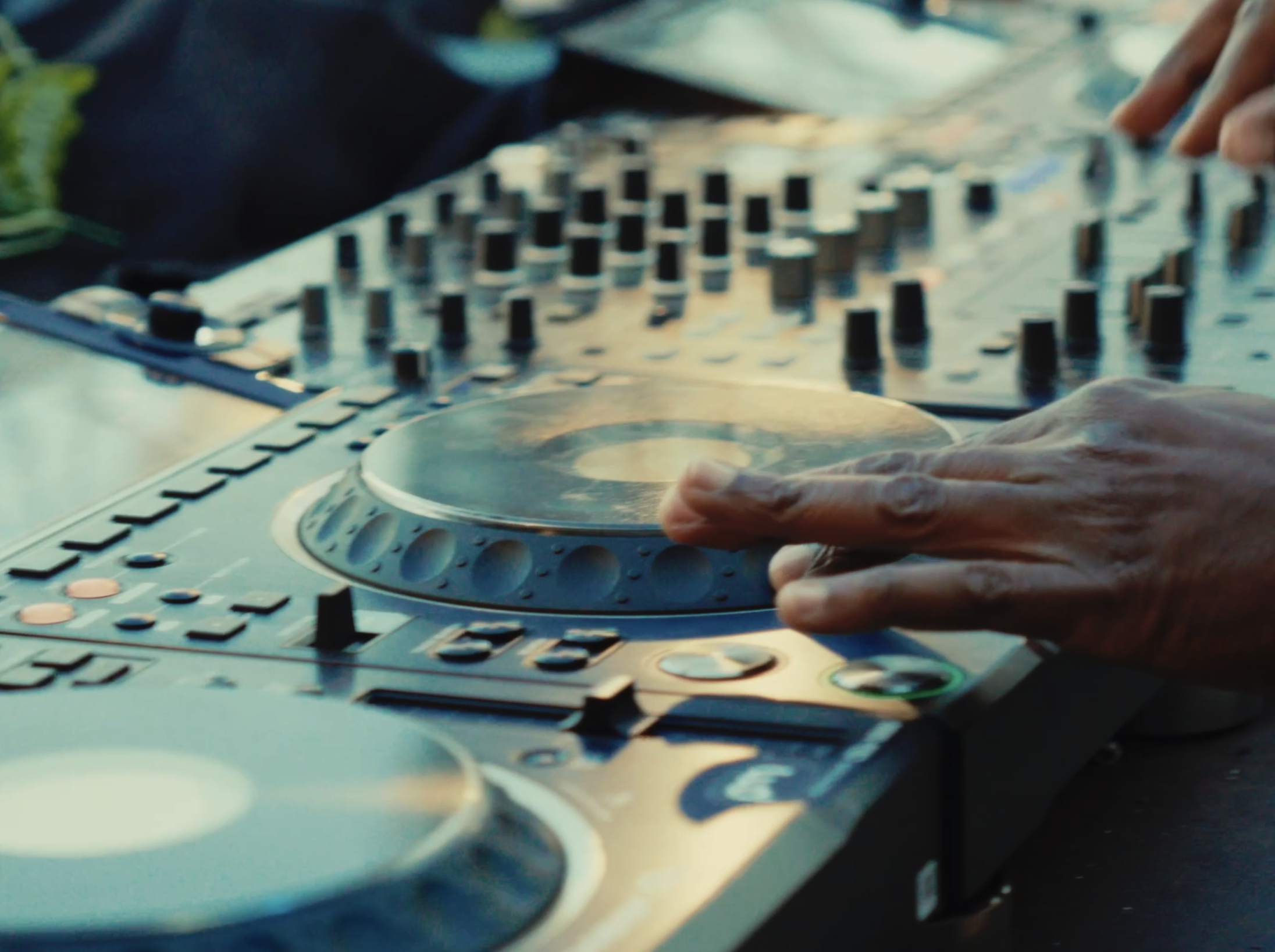Close-up of a DJ's hand adjusting equipment on a professional DJ controller with multiple knobs and turntables.