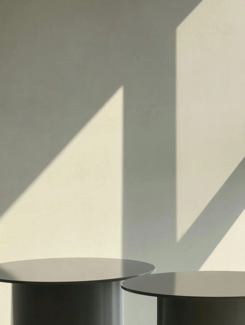 Two black furniture pieces with shadows on a light-colored wall, creating geometric shapes.