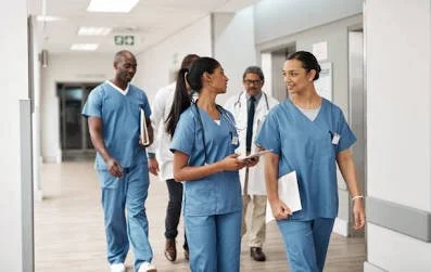Cuatro profesionales de la salud en un pasillo del hospital, dos de ellos en uniforme de enfermería y los otros dos con batas blancas y gafas.