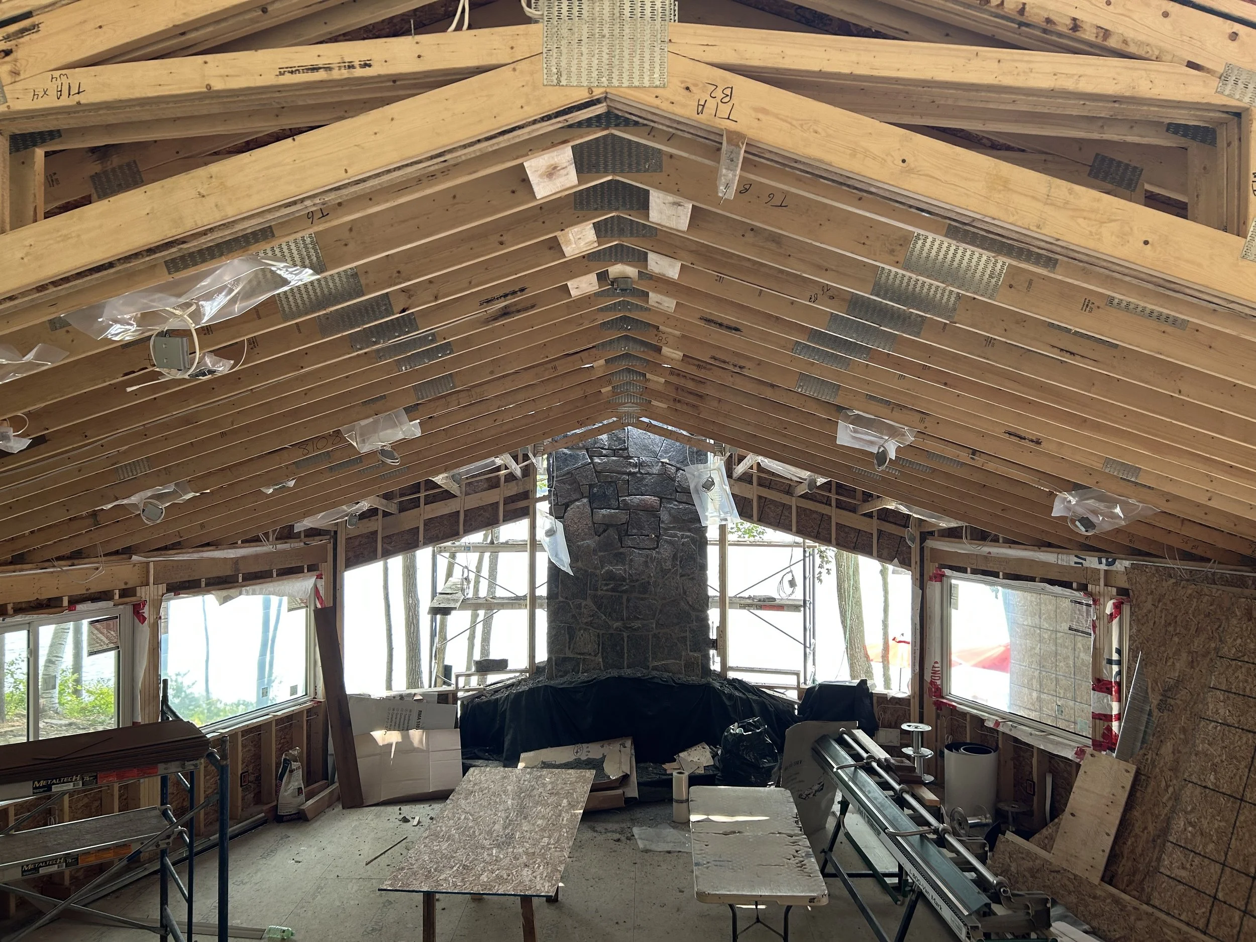 The interior of a house undergoing construction with exposed wooden framing, a stone chimney, construction tools, and scaffolding. Home electrical services provided by Muskoka electrician, Clearwater Electric.