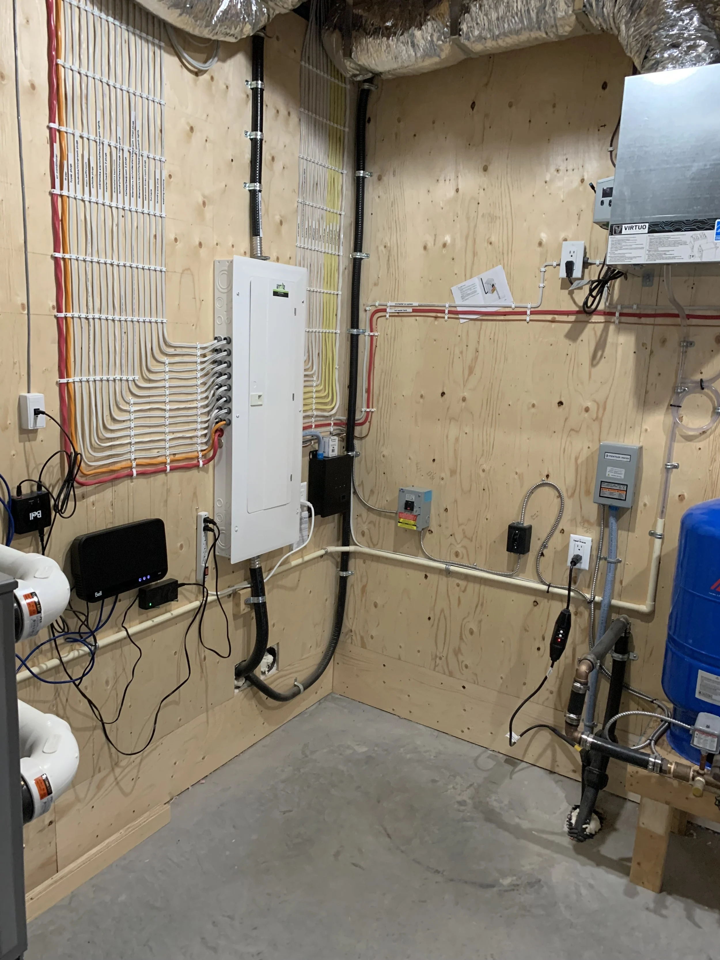 Electrical job by Clearwater Electrical. A utility room with electrical and plumbing components installed on wooden walls, including pipes, boxes, and a blue water pressure tank.