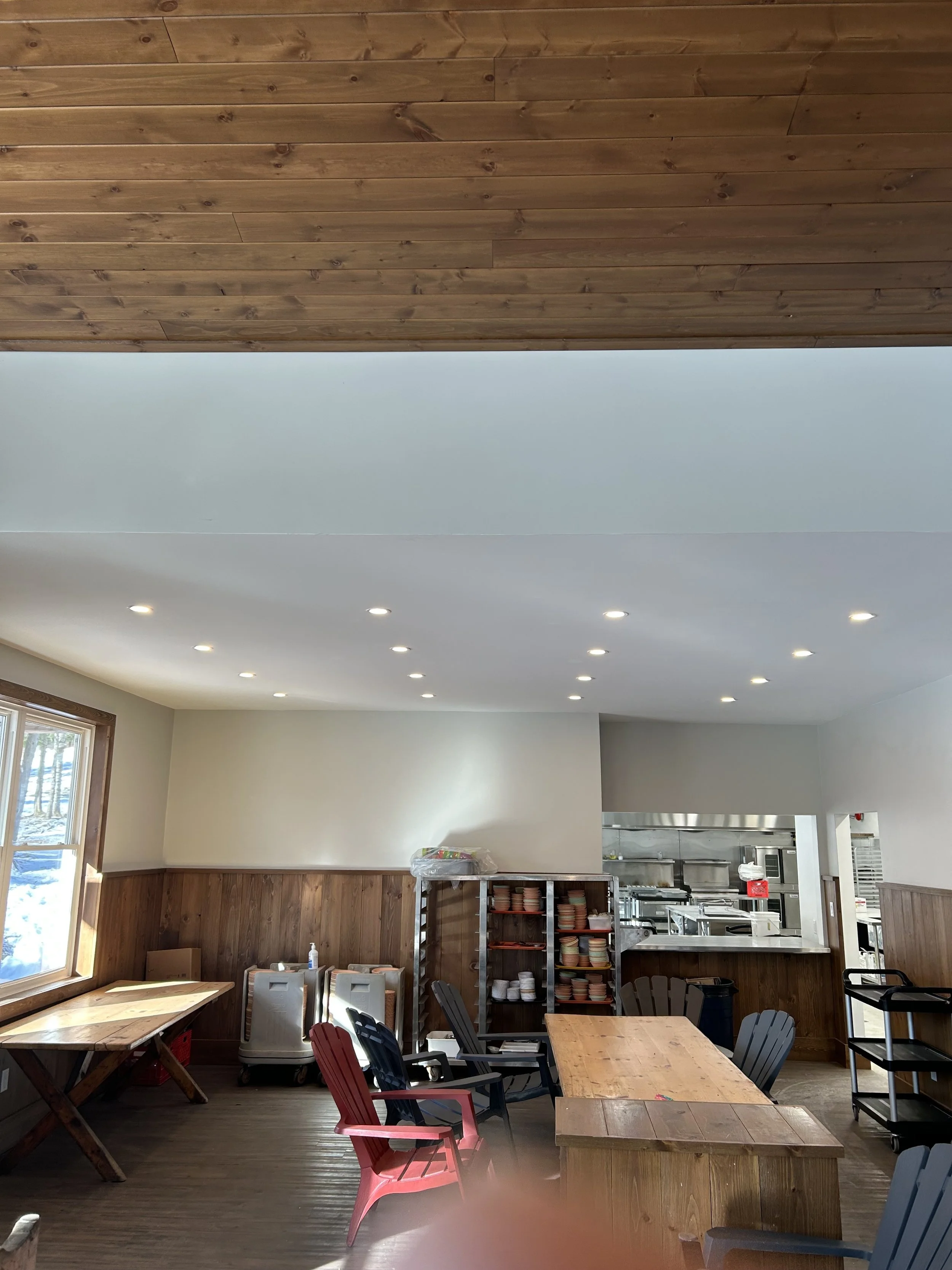 Electrical installation by Clearwater Electric. Interior of a dining area with wooden walls, large window, tables, and chairs, and an open kitchen in the background.