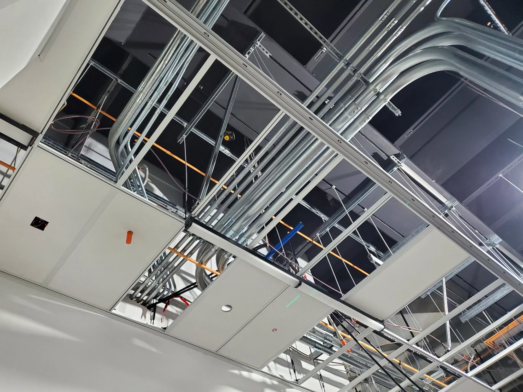Ceiling with exposed electrical conduits, pipes, and unfinished drywall in a construction site. Industrial electrical services provided by Muskoka electrician, Clearwater Electric.