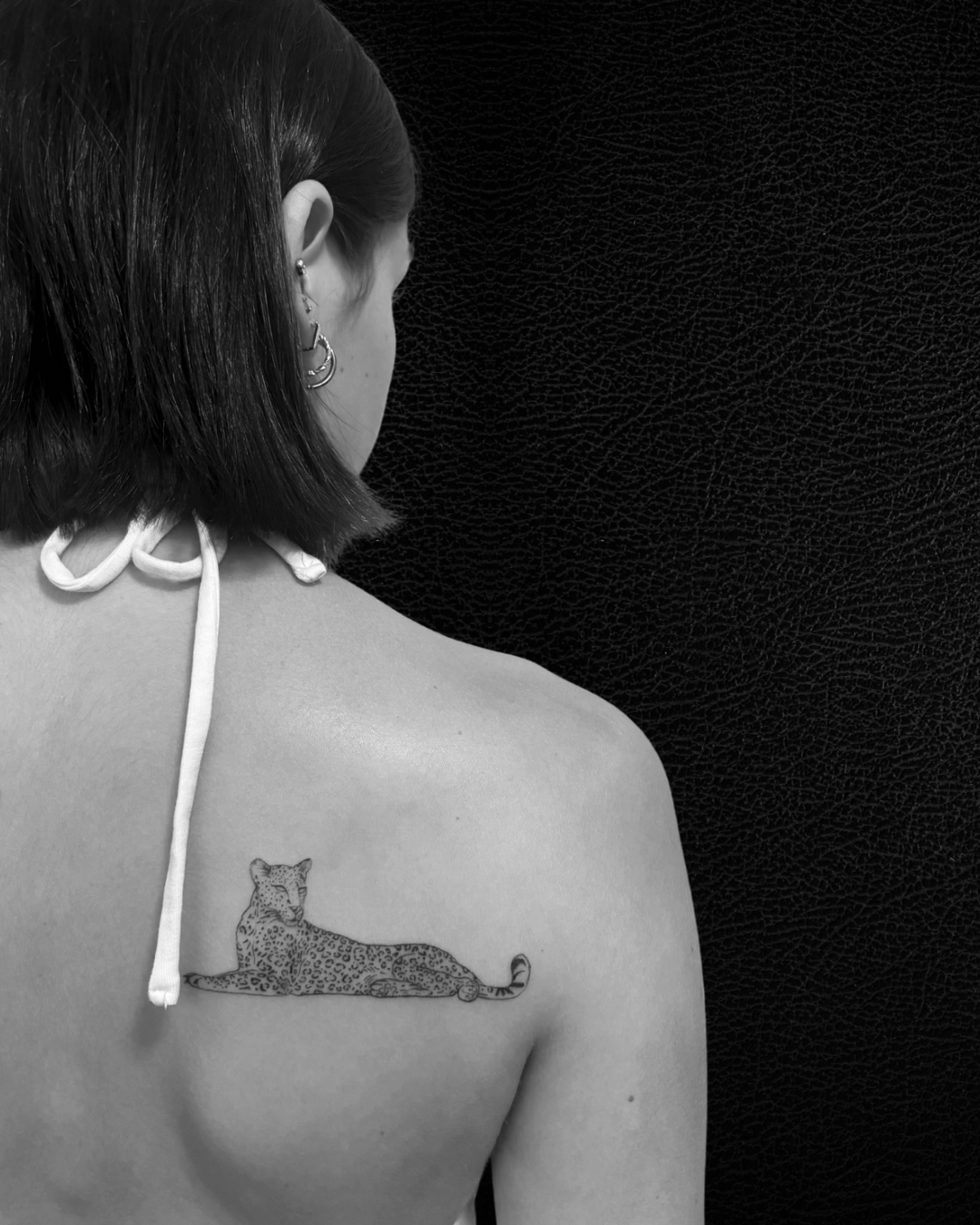 Tatouage d'un léopard allongé sur l'épaule gauche d'une femme, vue de dos.