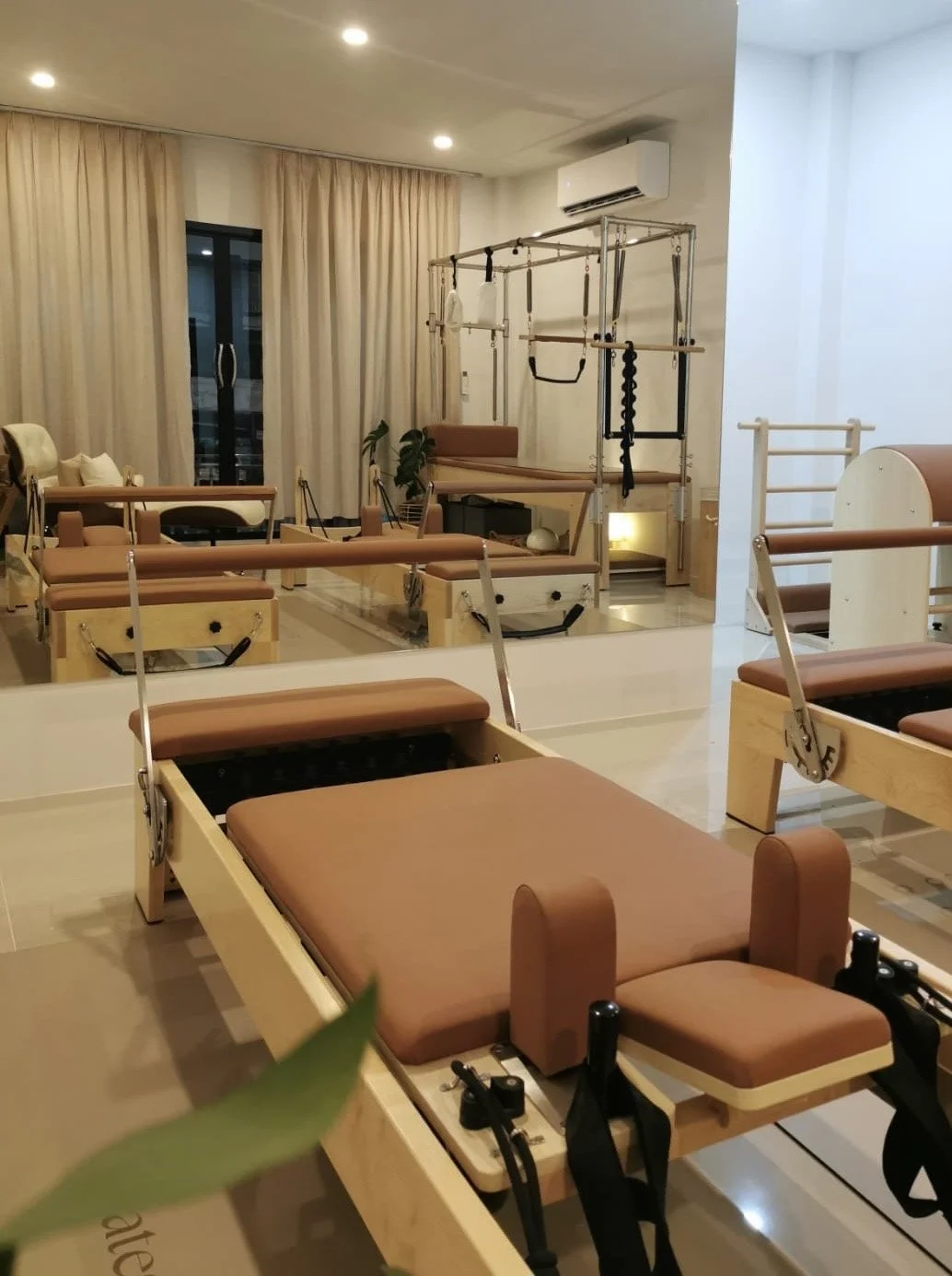 A therapy or Pilates studio with specialized equipment, including reformer machine, pilates chair, a wooden ladder, and various exercise apparatus.